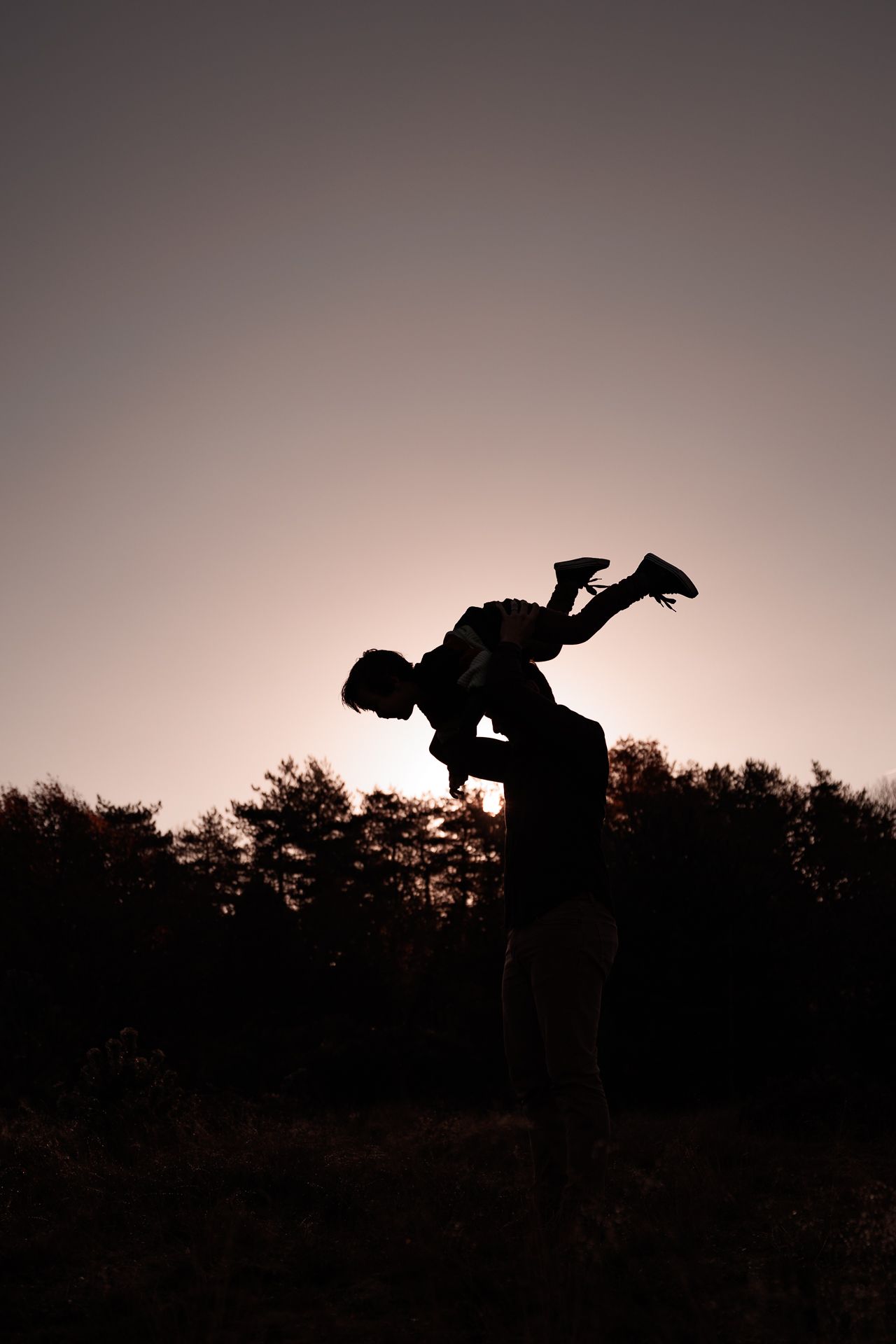 vader en zoon spelend tijdens fotoshoot waarbij vader zijn zoontje in de lucht houdt