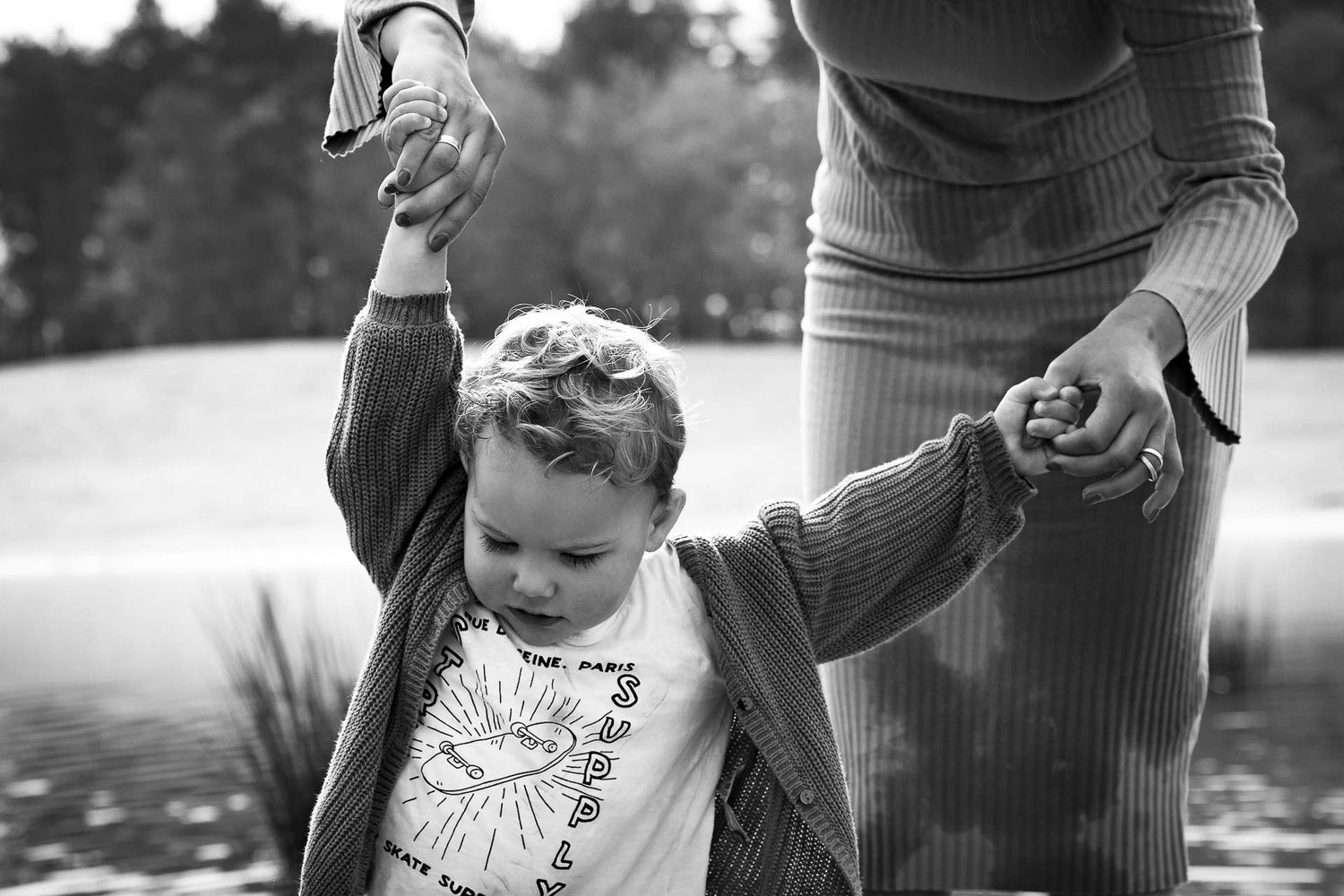 spontaan moment waarbij kind de handen van moeder vasthoudt tijdens gezinsfotoshoot op een buitenlocatie aan het water