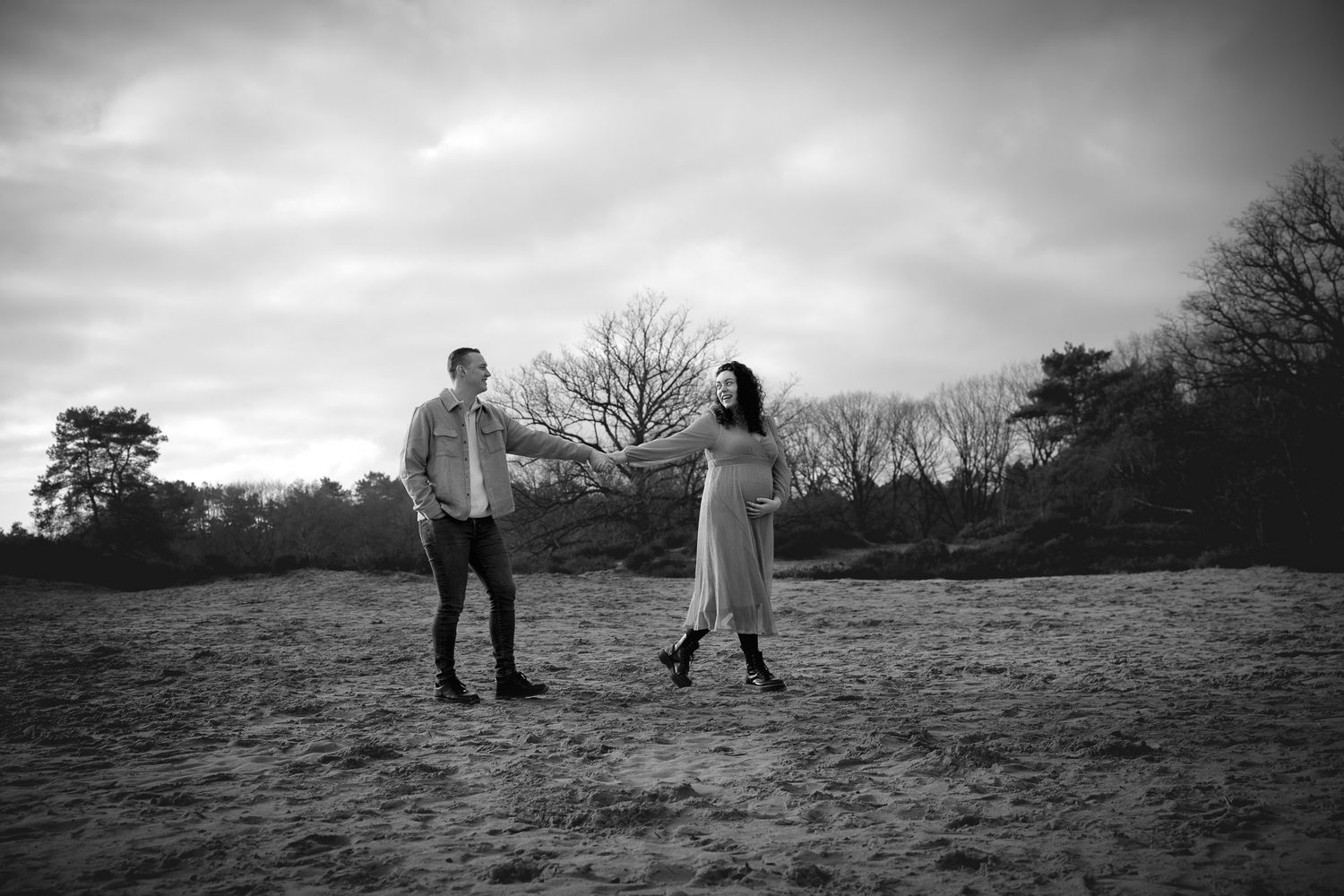 hand in hand trekt de zwangere vrouw de man met haar mee, vrolijk lachend en ontspannen tijdens fotoshoot op de heide