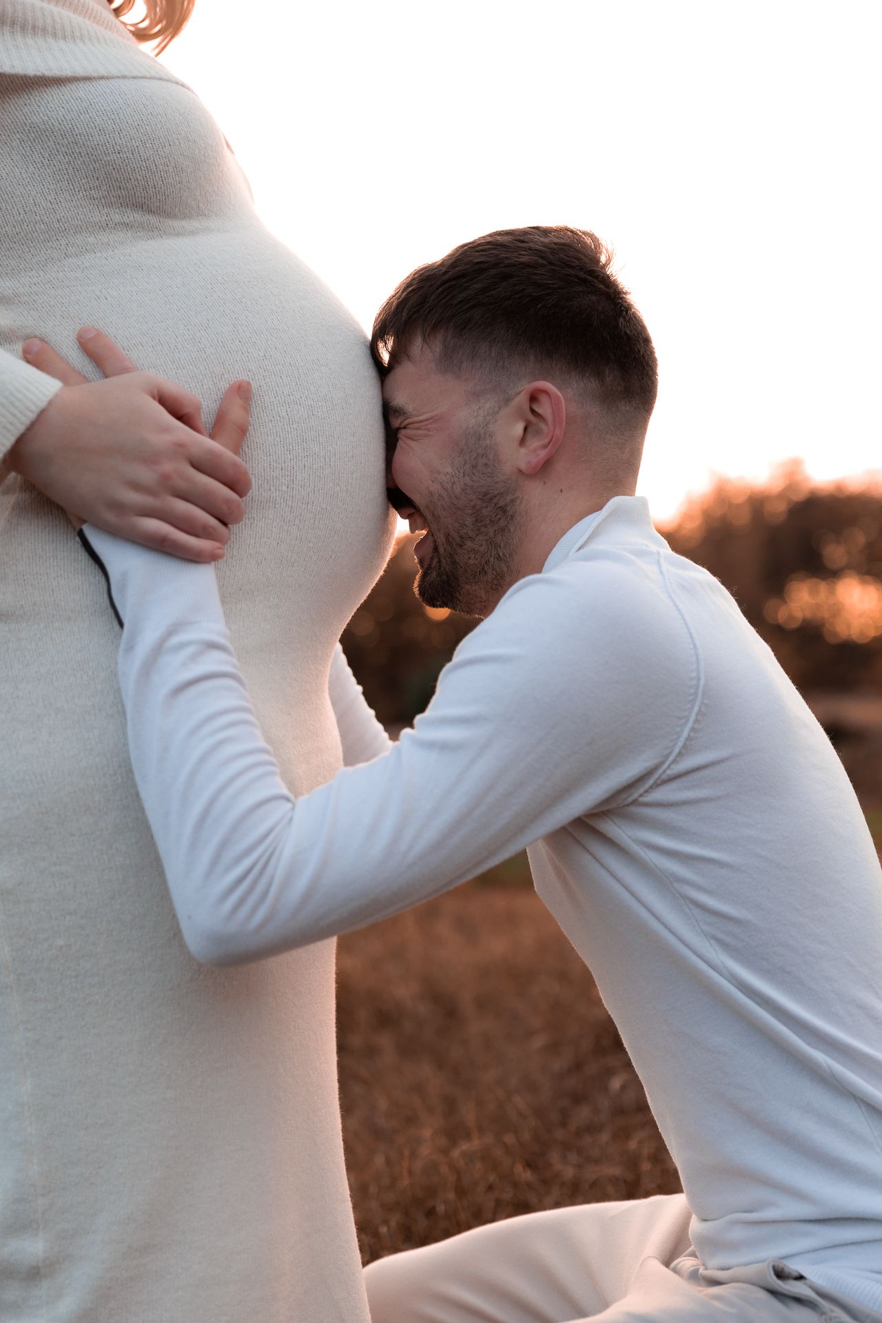 grappige foto van aanstaande vader die de buik van zijn vrouw vasthoud en lief lacht