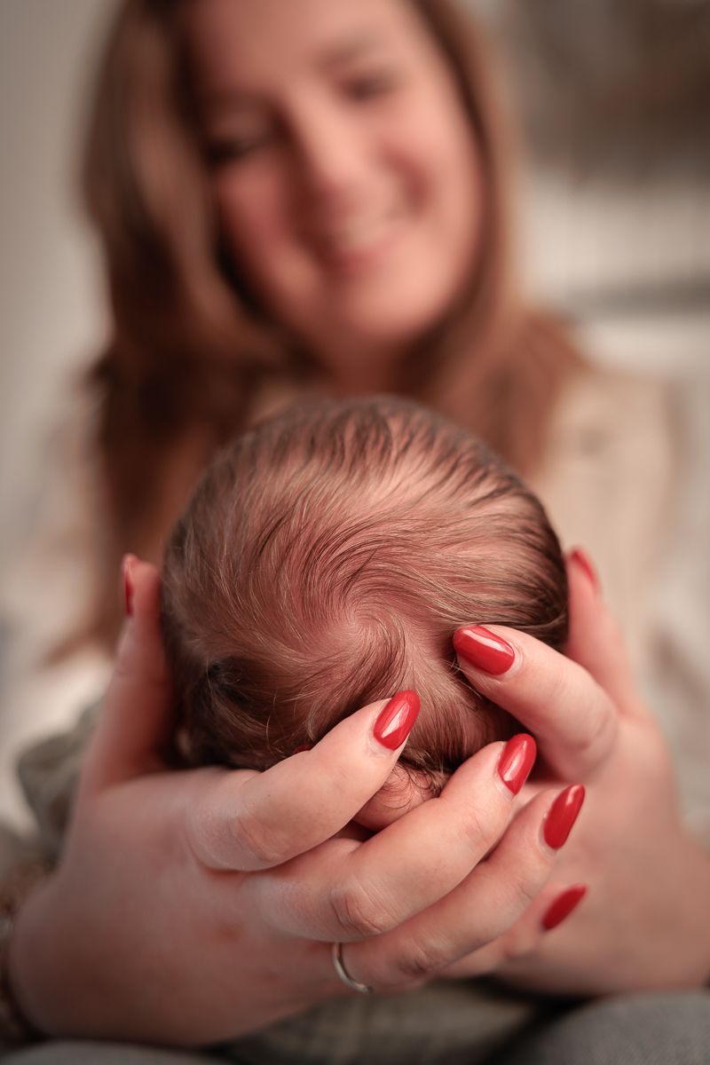 Newborn babyhoofdje in handen van mama tijdens newbornshoot thuis