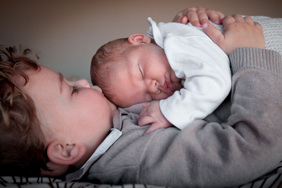 grote broer met newborn broertje op zijn buik, thuis op ouderlijk bed tijdens  newborn fotoshoot