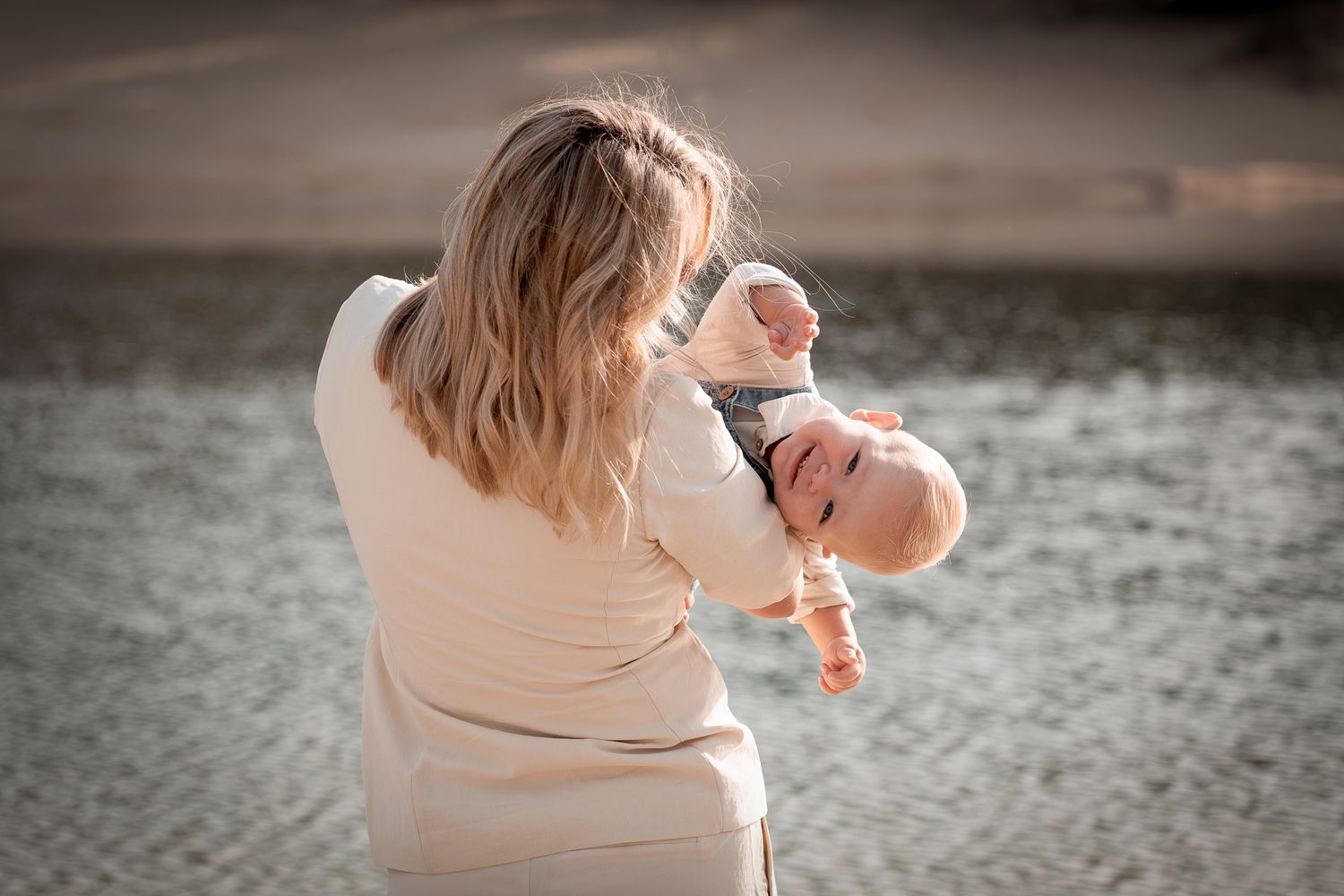 moeder en baby met water op de achtergrond, spelend en lachend tijdens fotoshoot