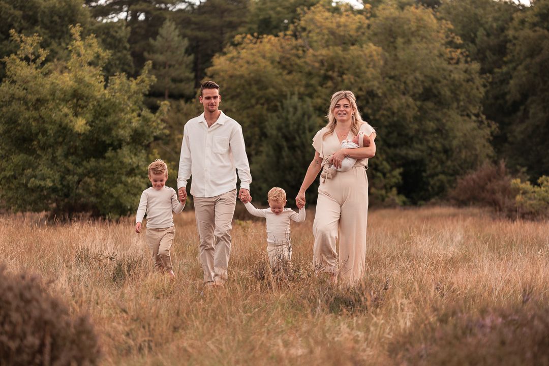 jong gezin lopend naar de fotograaf, hand in hand met elkaar. buiten in de natuur