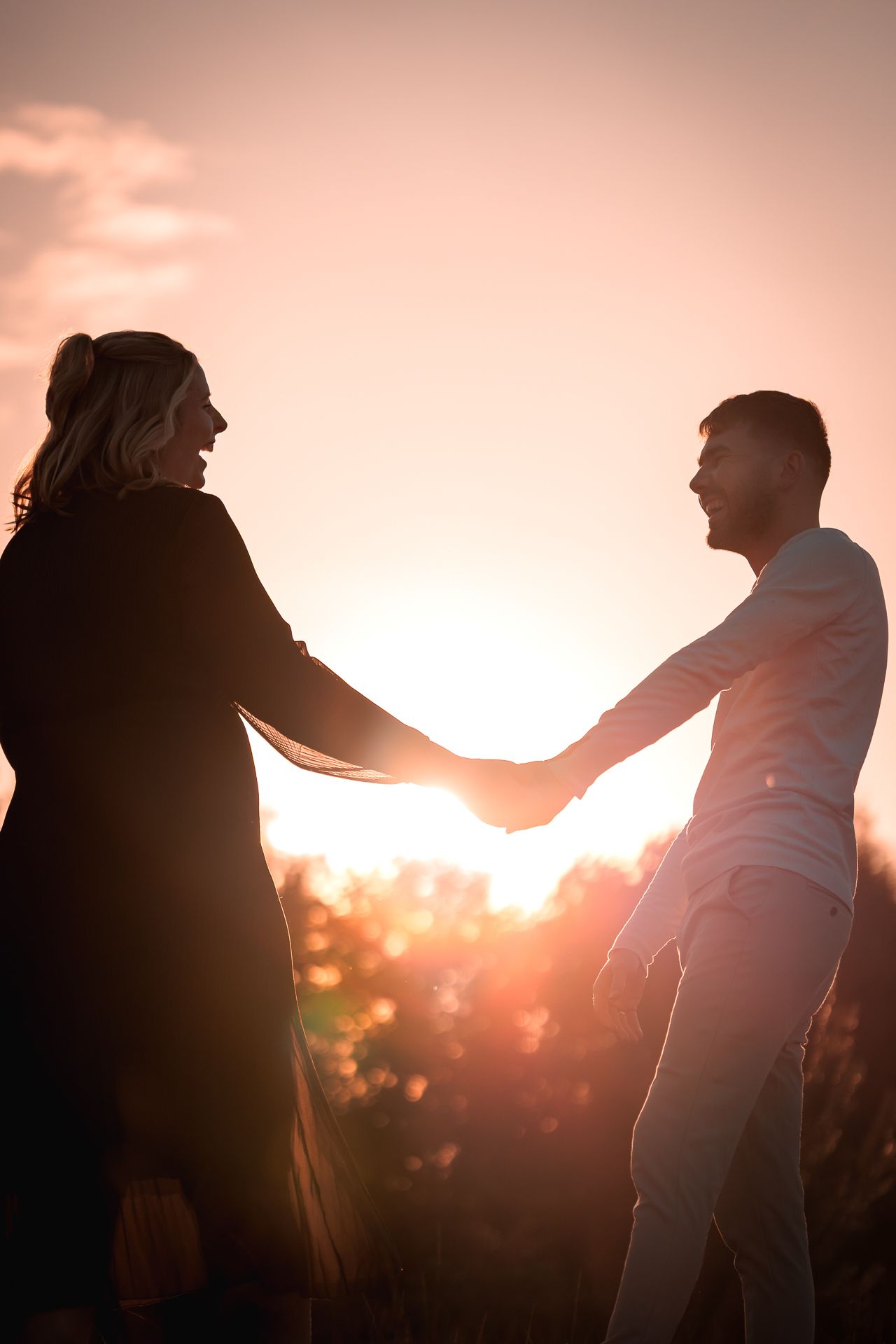 zwangerschapsfotoshoot tijdens het golden hour partners hand in hand lachend naar elkaar