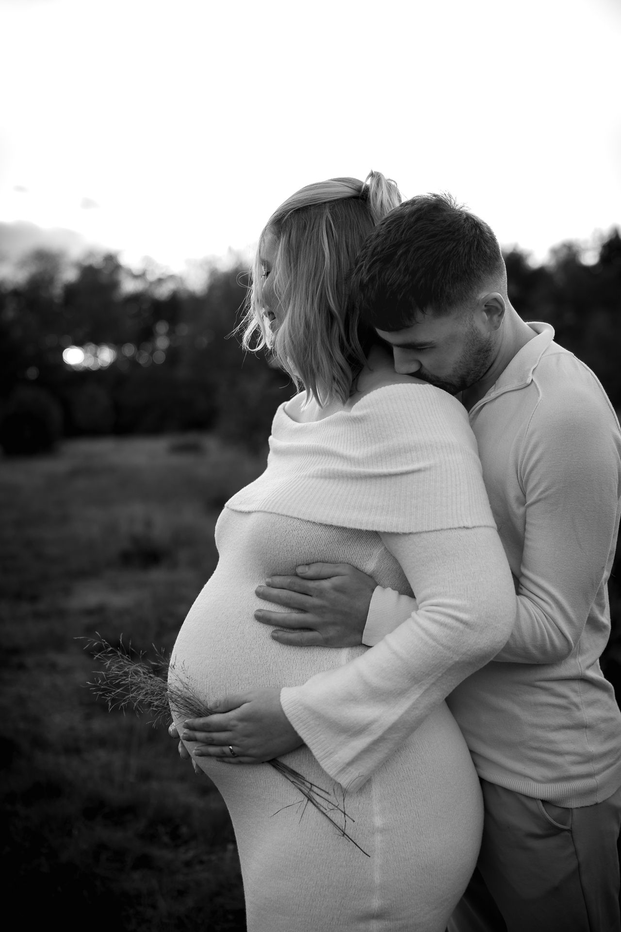 innige omhelzing waarbij de man de zwangere vrouw op haar sleutelbeen kust tijdens buitenfotoshoot in Bergen op Zoom