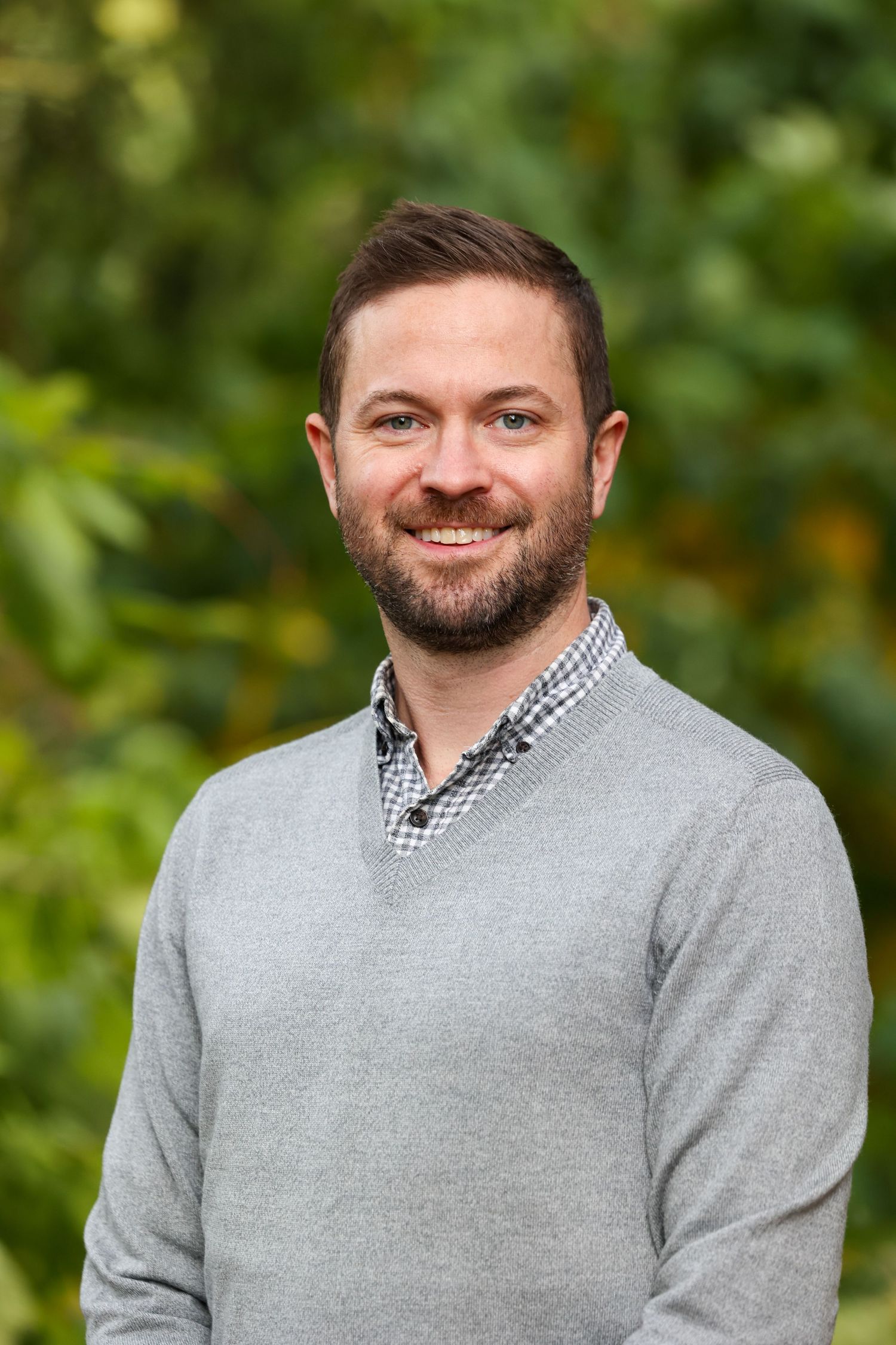 Professional headshot portrait of person wearing grey sweater and checkered collared shirt outdoors in Chicago