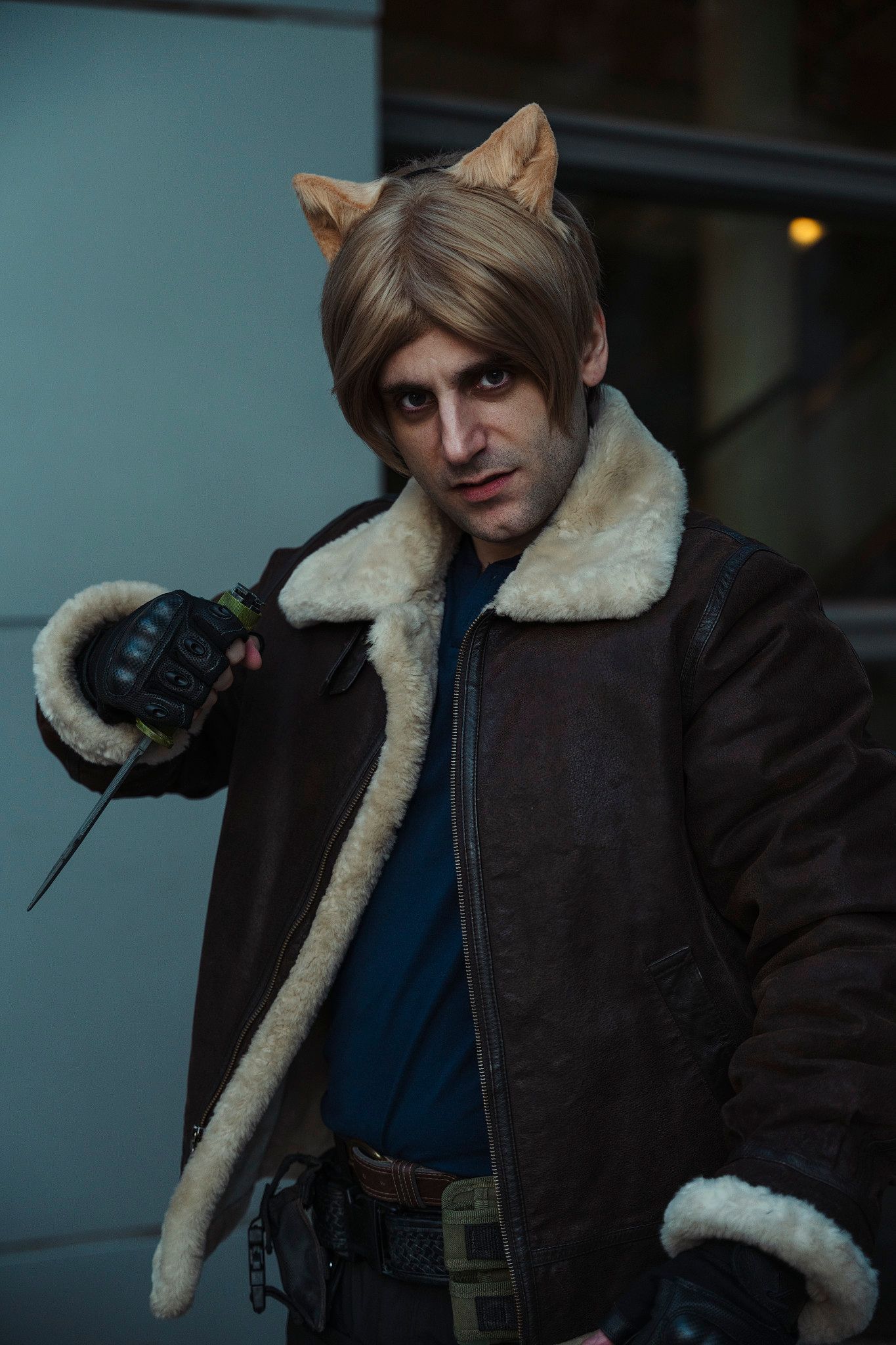 A man cosplaying as a cat-human hybrid character holds a grenade in a dramatic indoor pose.