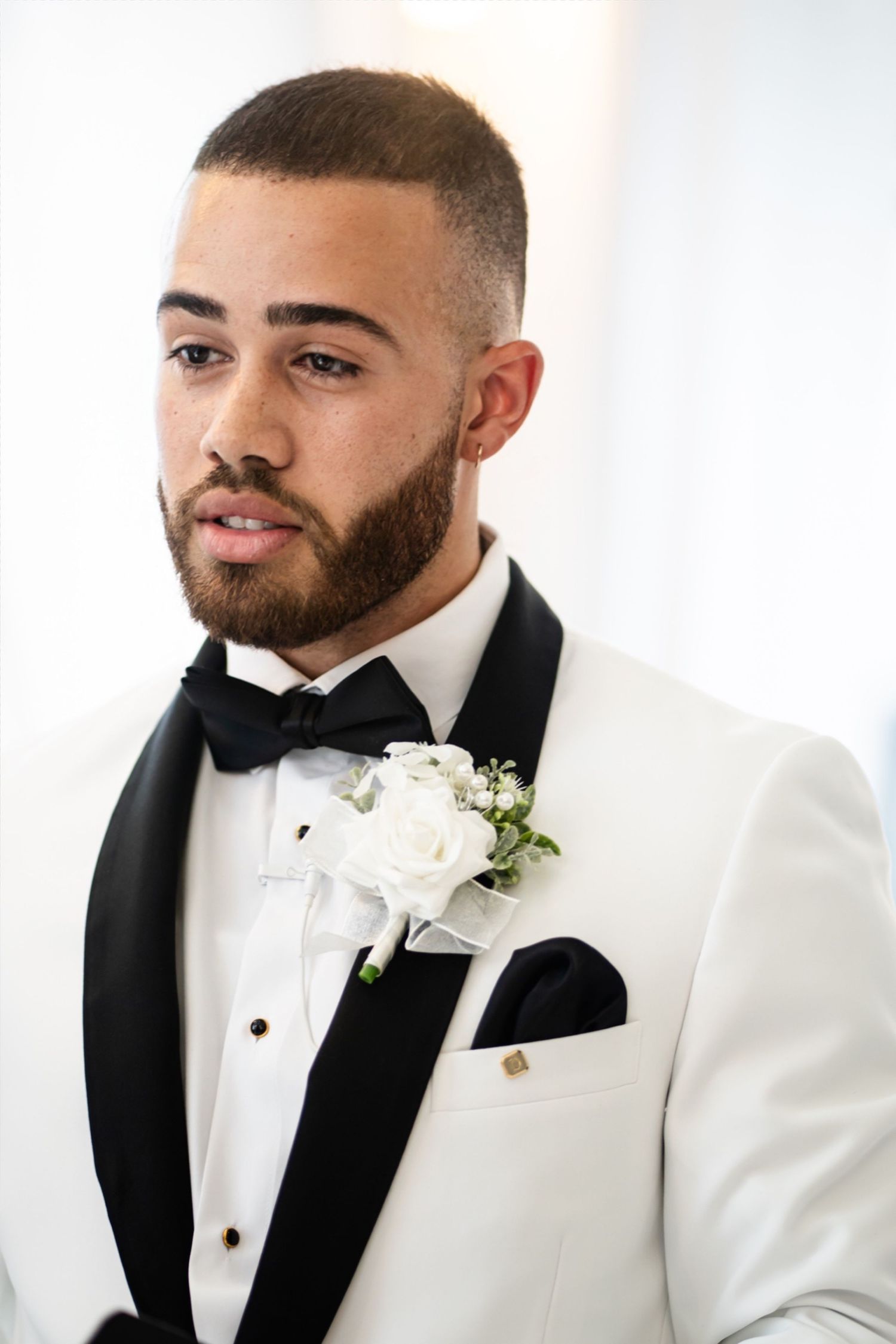 Groom in white tuxedo with black lapels and bow tie poses for formal wedding portraits.