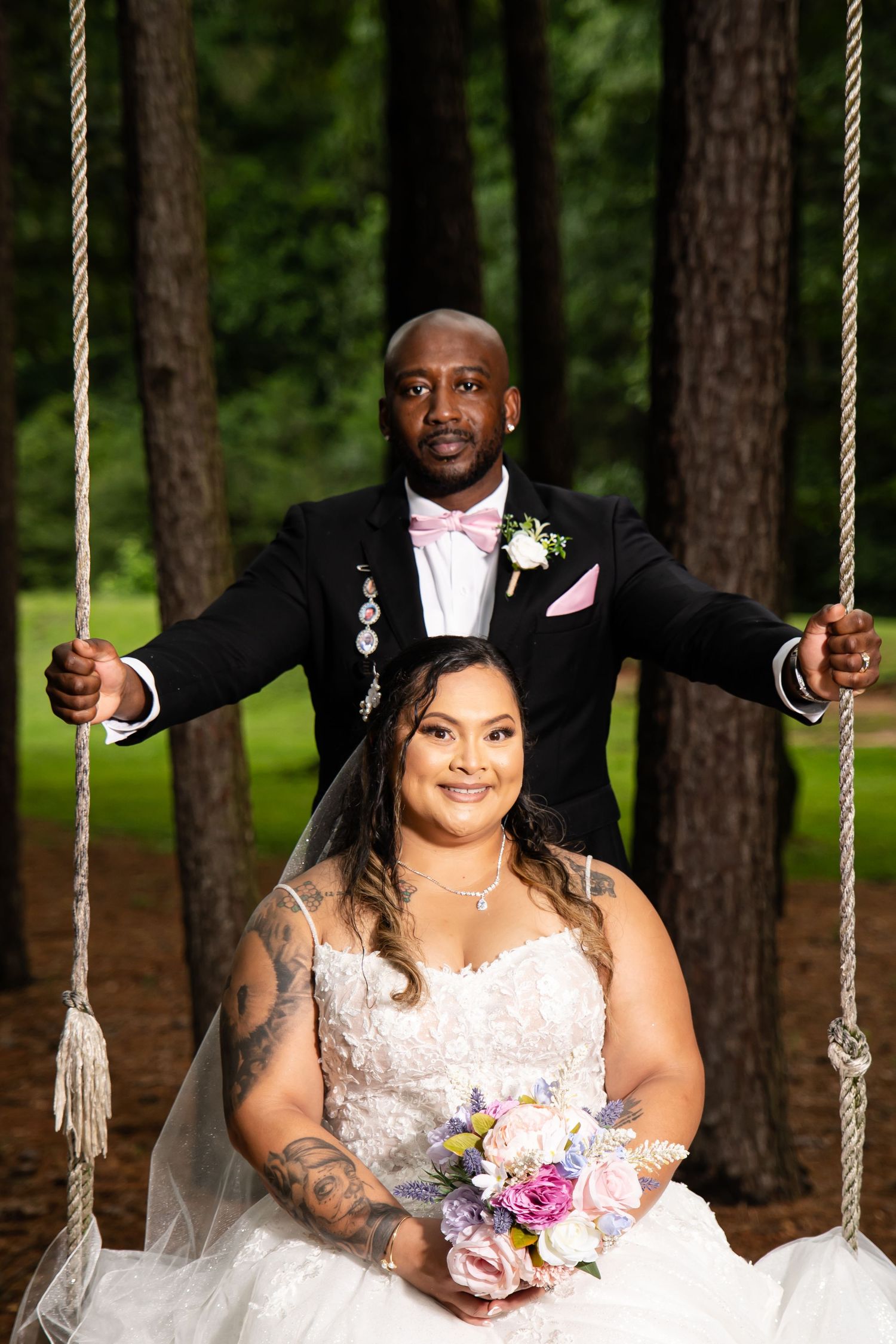 Wedding party posing on rope swings in a wooded outdoor setting.