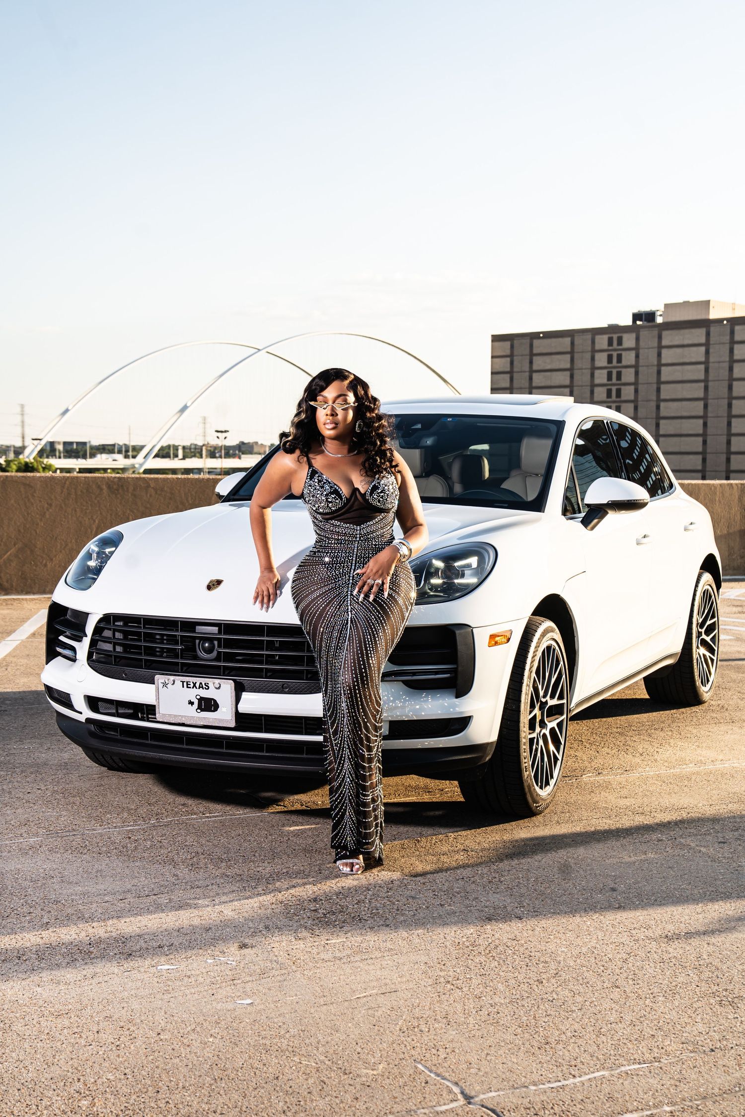 Glamorous photoshoot with a white luxury car on a rooftop parking deck at sunset.