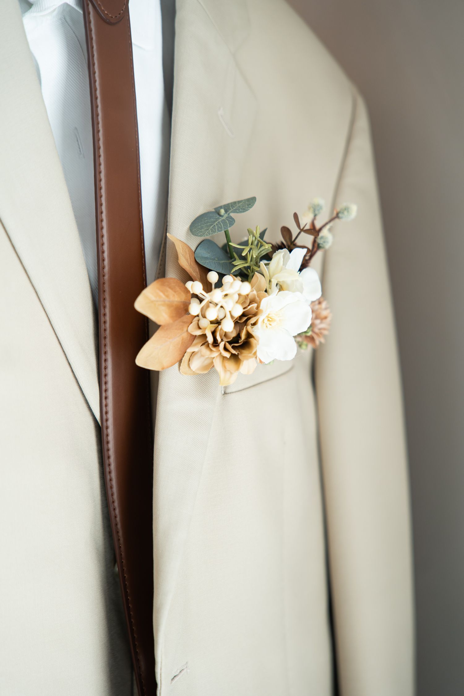 Close-up of cream colored suit jacket with peach and white floral boutonniere.