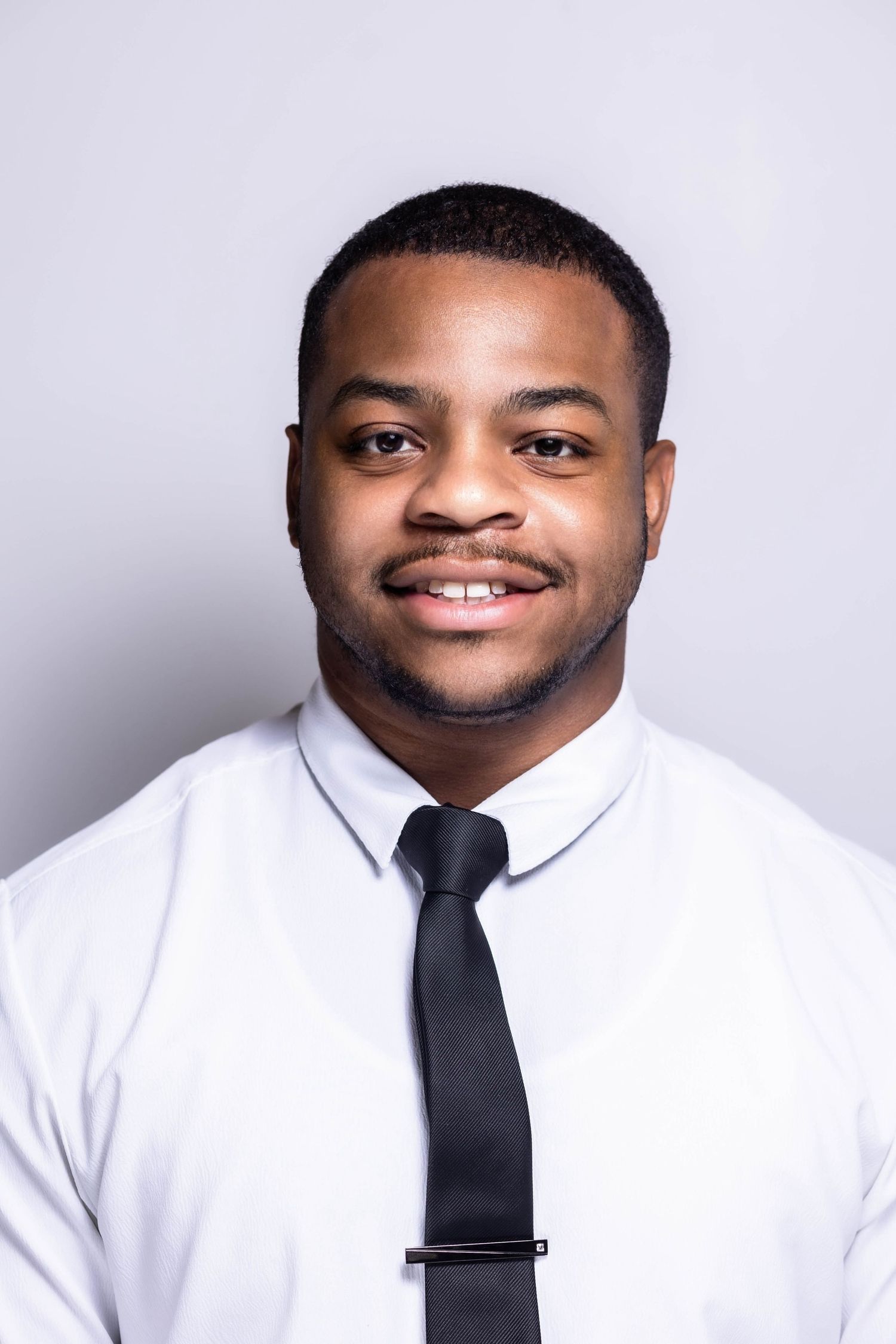 Professional headshot of a person in white dress shirt and black tie smiling at the camera.