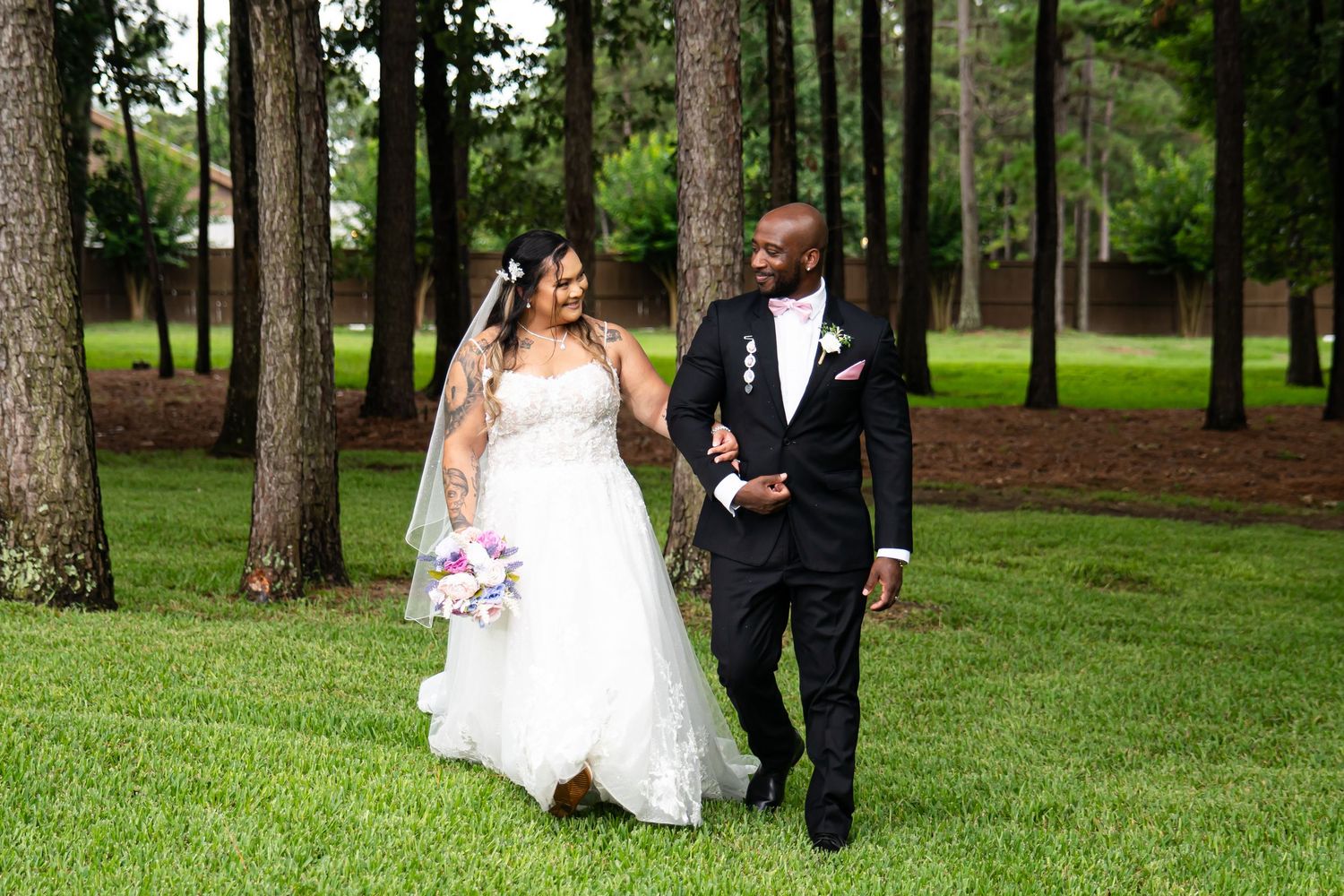 Bride and groom walking together through a serene pine forest setting.