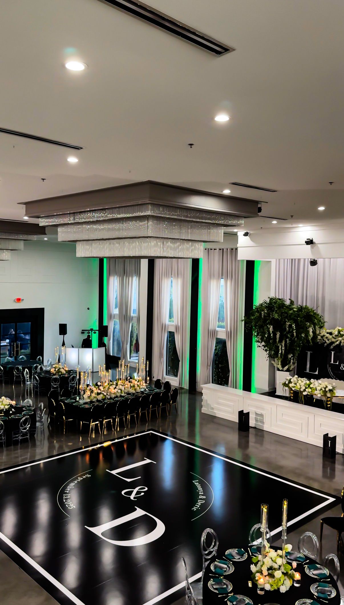 Modern wedding reception venue with black dance floor and green accent lighting.