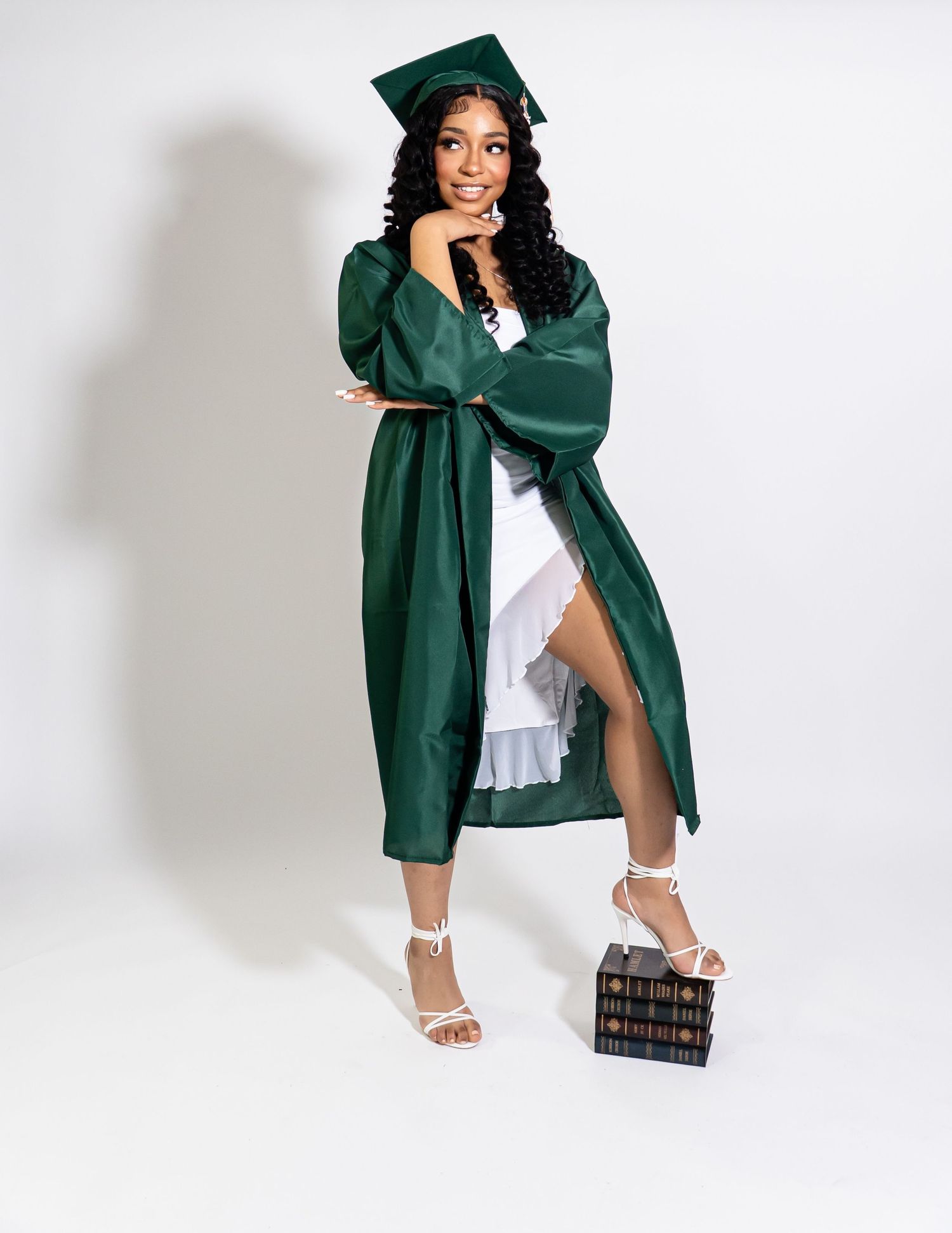 Graduation photoshoot featuring poses with cap, gown and white dress against studio backdrop.