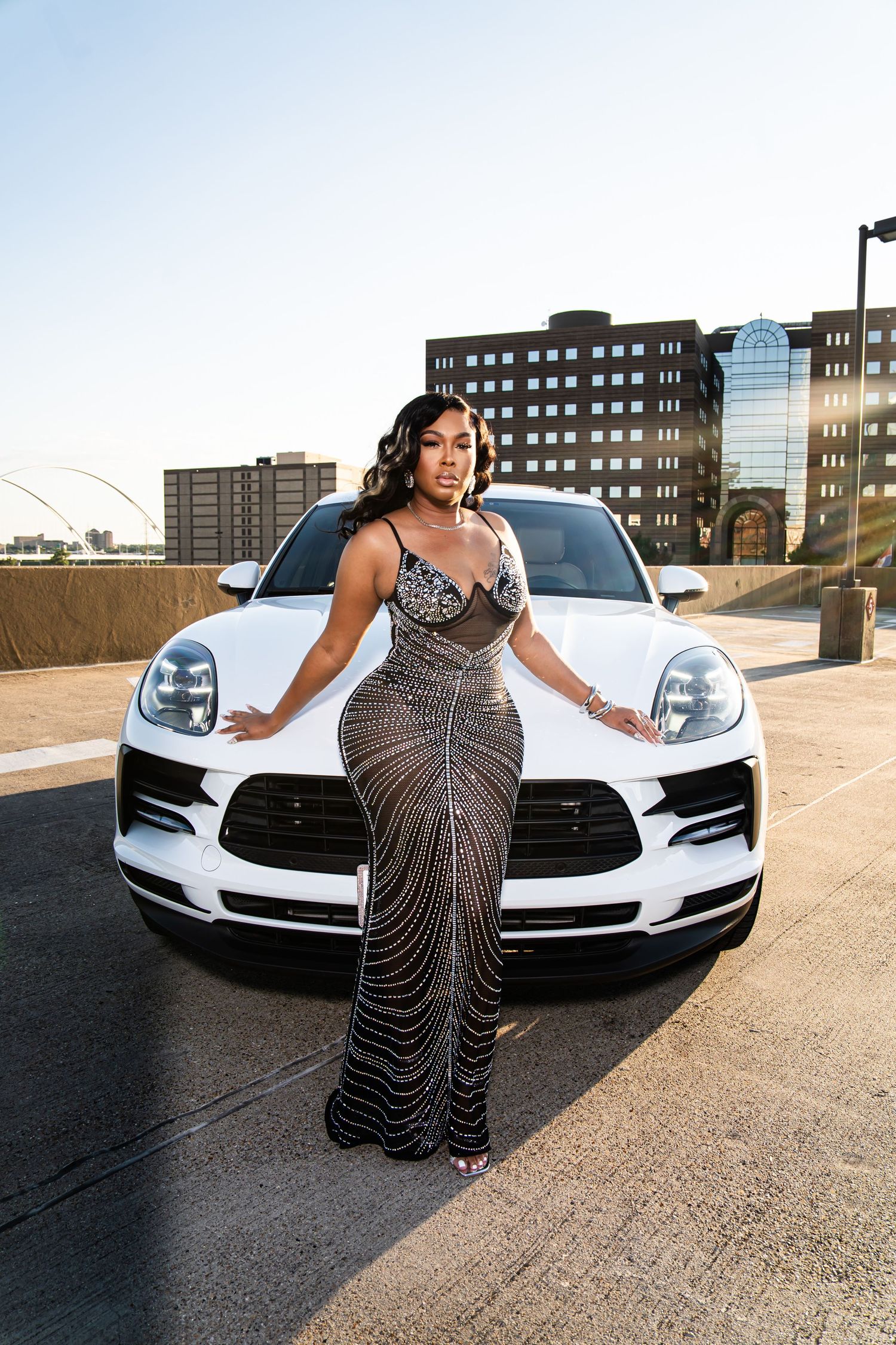 Fashion model poses with a white Porsche sports car in an urban setting.
