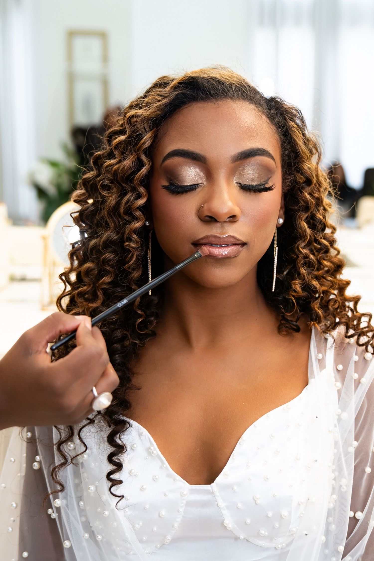 Bride getting ready with professional makeup application showing different angles in white dress with curly hair.
