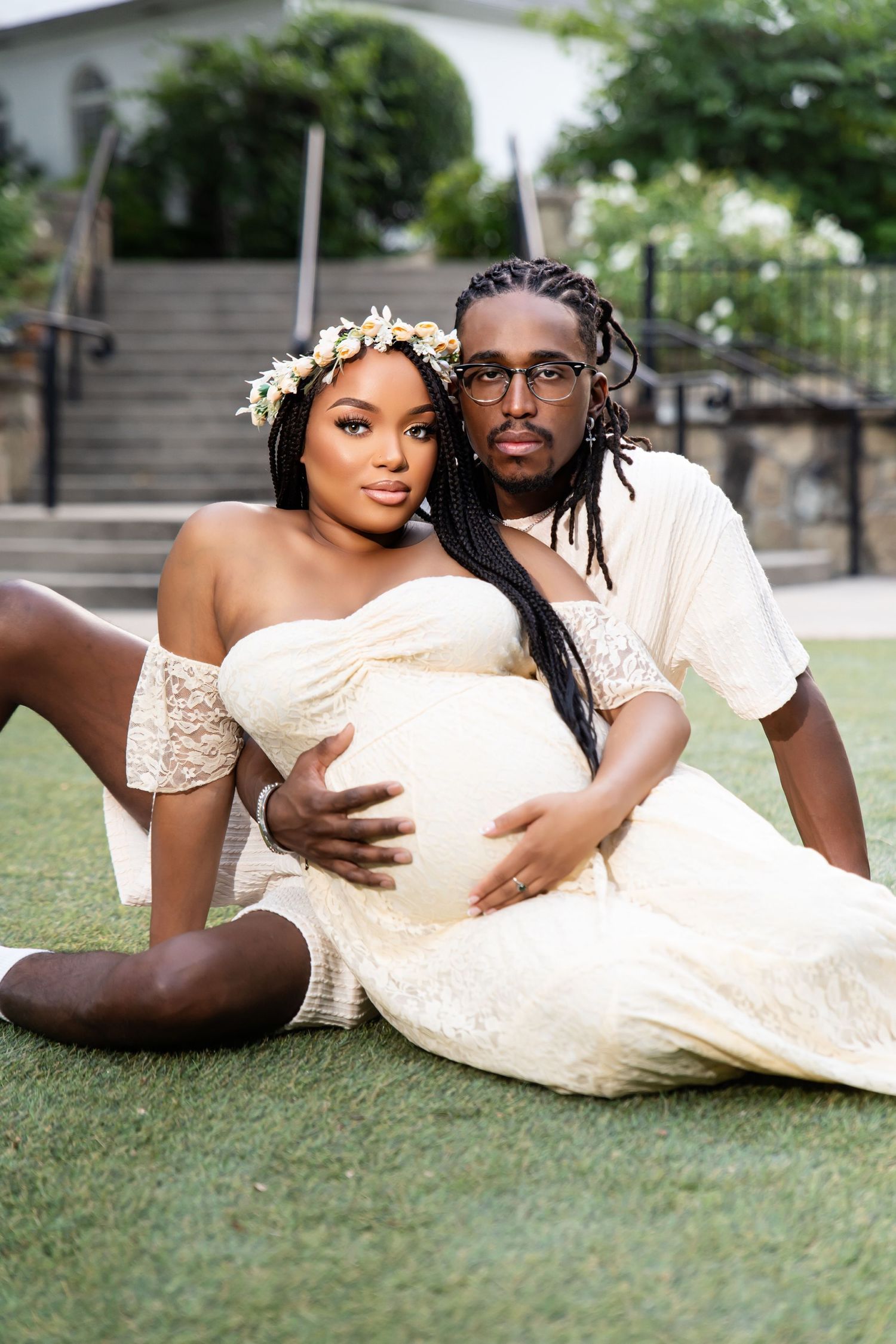 Romantic maternity photo of couple in white outfits lounging on grass.