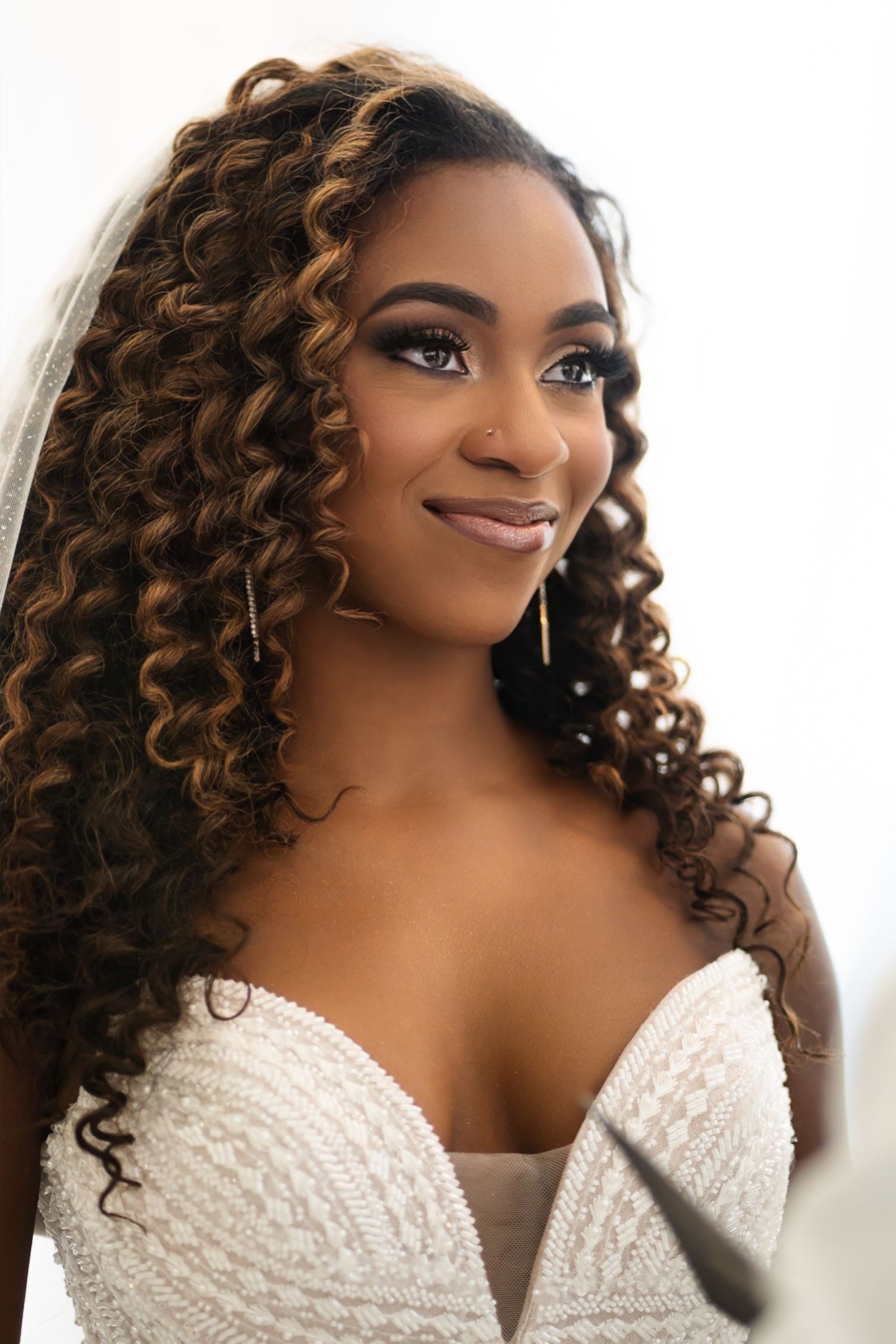 Beautiful bridal portrait featuring curled hair and a detailed white wedding gown.