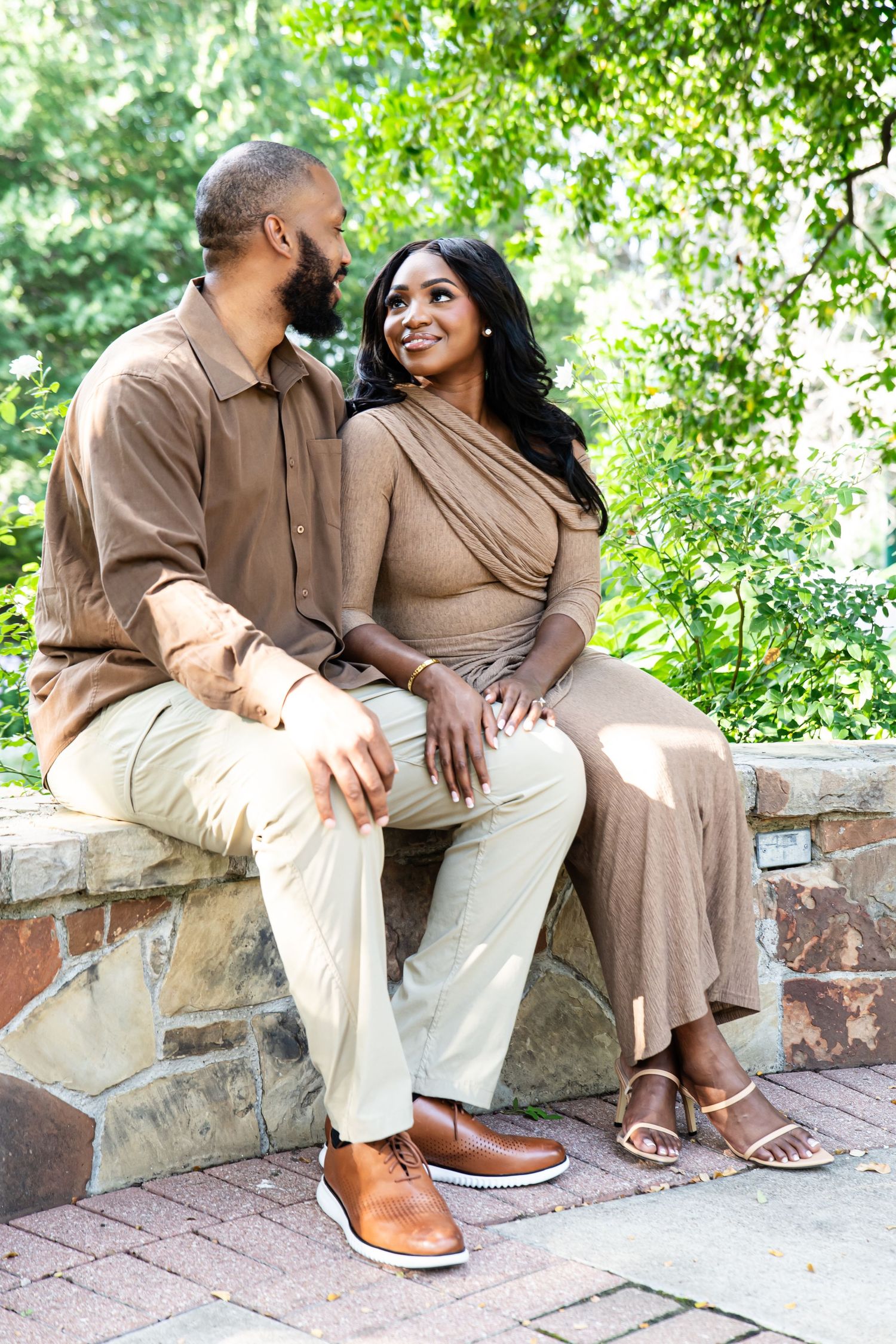 Couple in earth-toned outfits sitting together on stone steps in a garden setting.