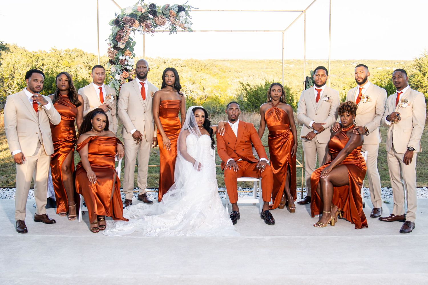 Wedding party in coordinated orange and cream formal attire posing outdoors.