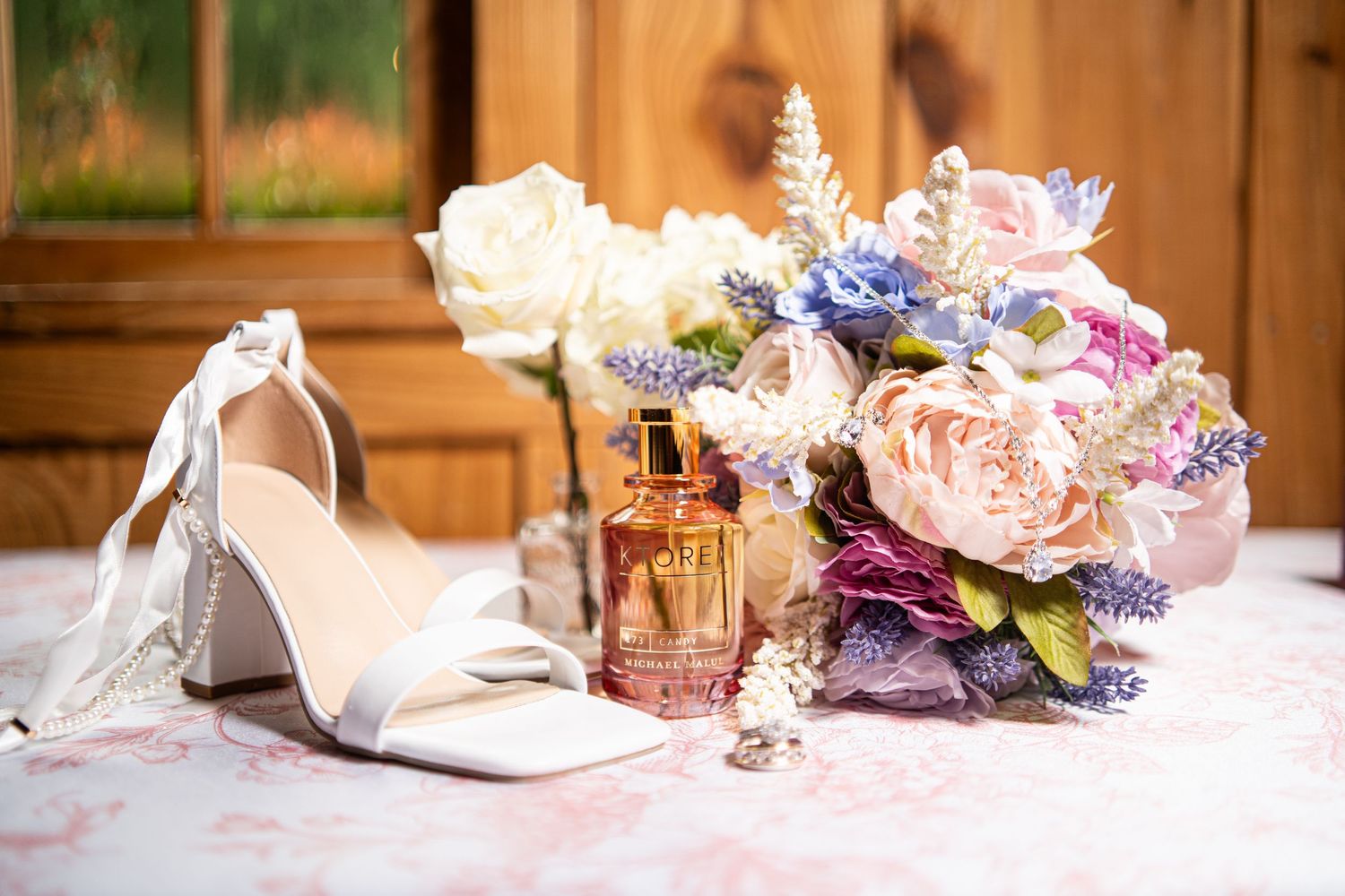 Wedding accessories including bouquet, shoes, and perfume arranged on wooden surface.
