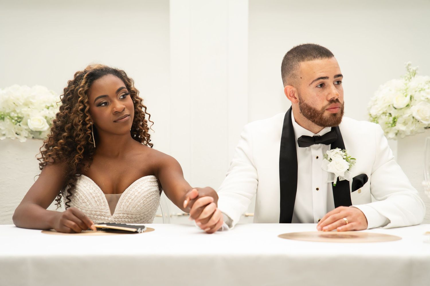 Wedding party seated at long white table during reception celebration.