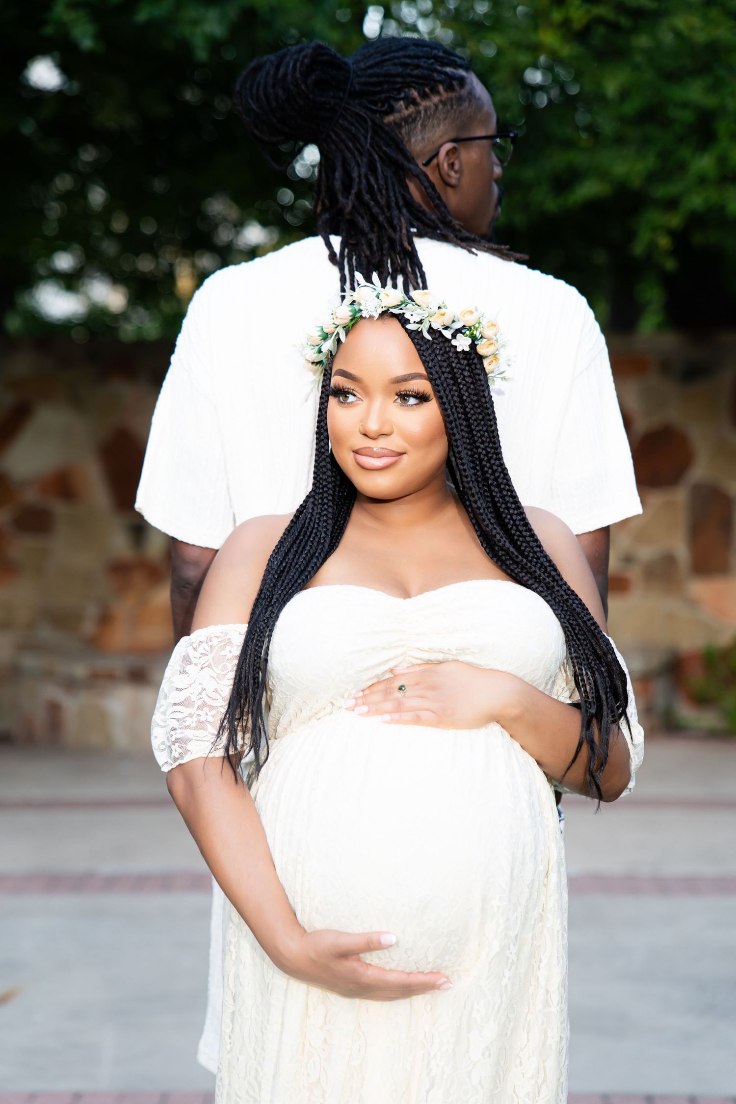 Artistic maternity portrait showing couple in white clothing against garden backdrop.