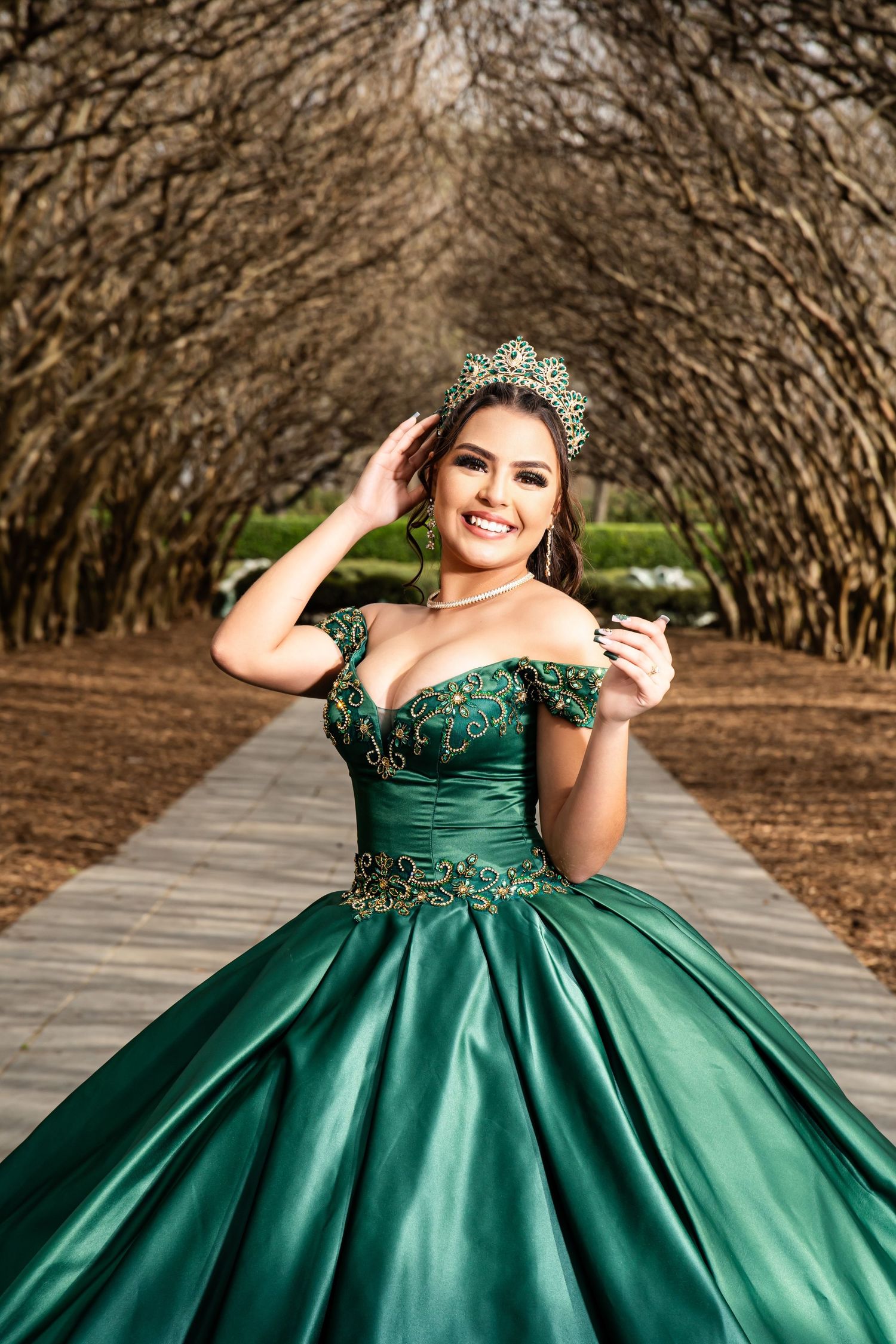 Emerald green ball gown photographed under an archway of trees with natural lighting.