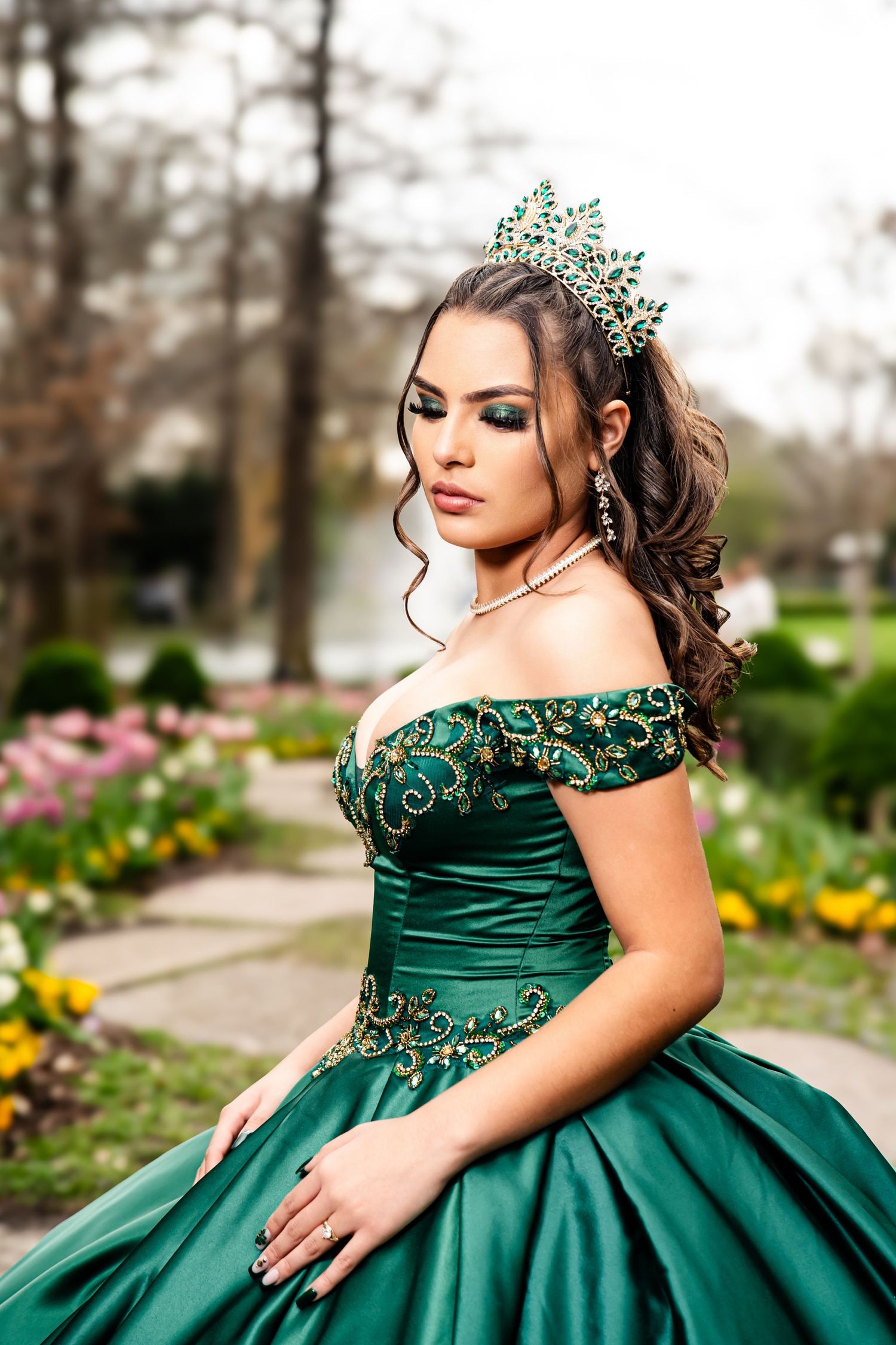 Emerald green quinceañera dress with ornate beading photographed in a garden setting.