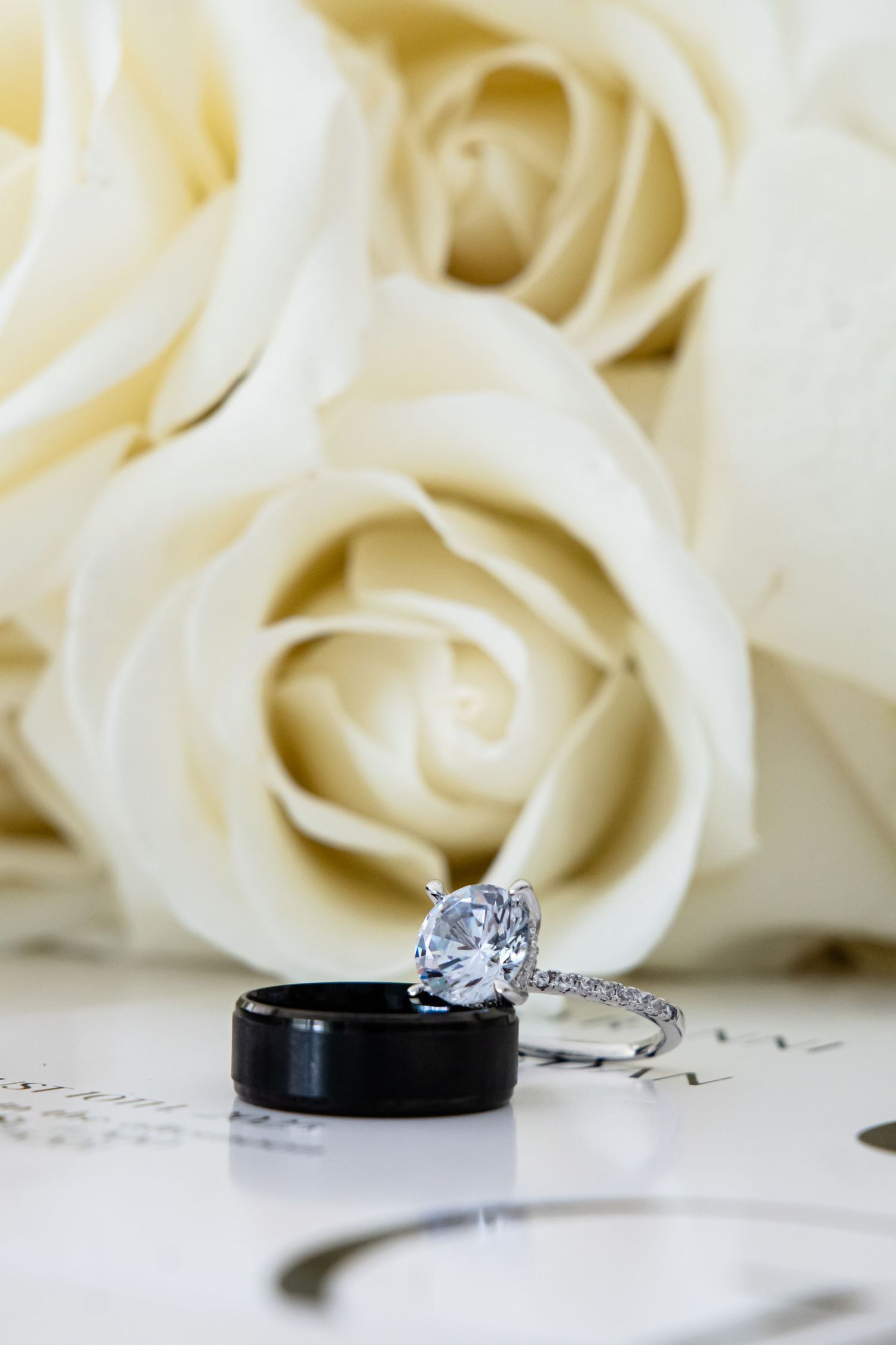 Wedding rings and diamond engagement ring displayed with white roses in the background.