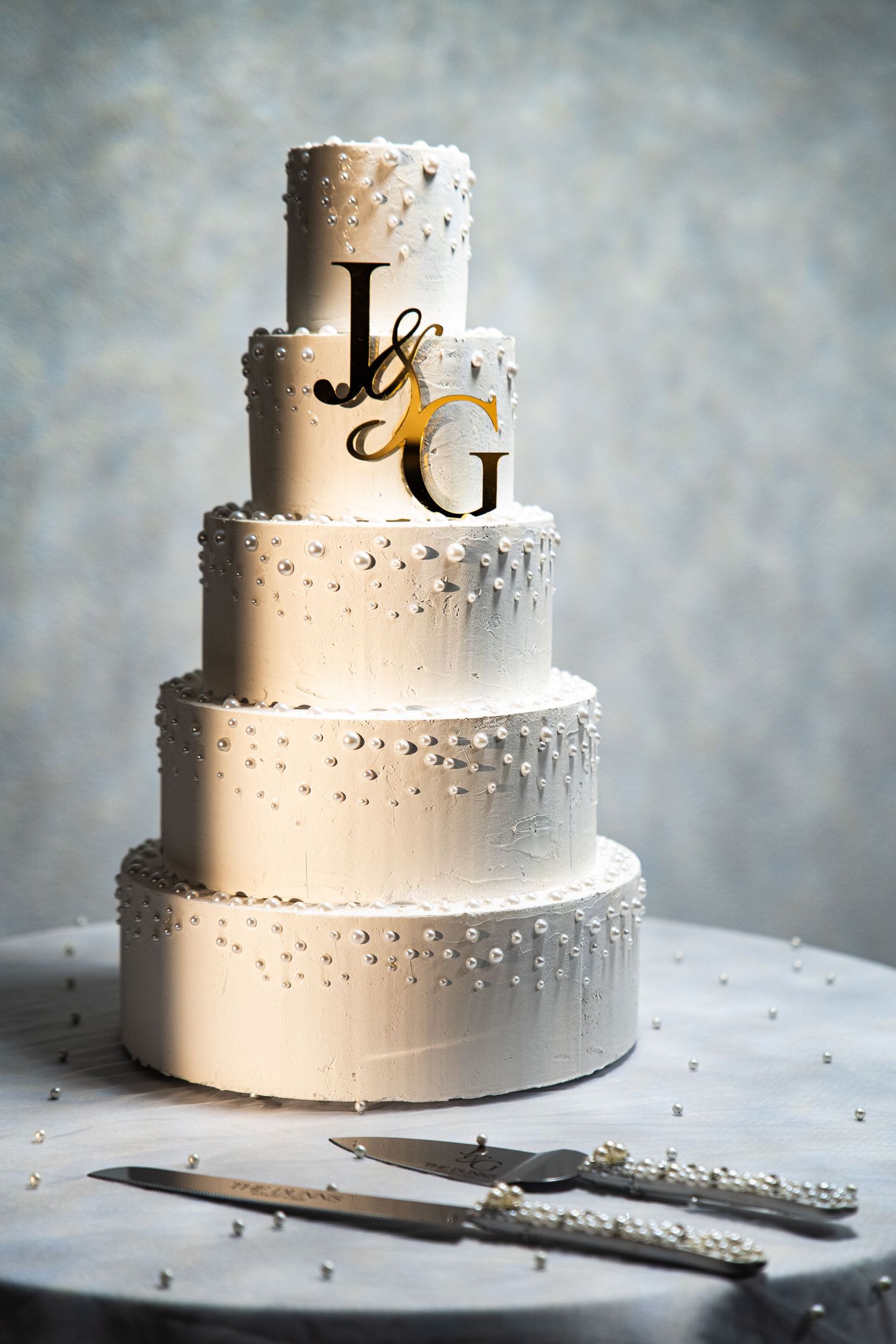 Elegant white wedding cake with monogram topper and silver accents on display.