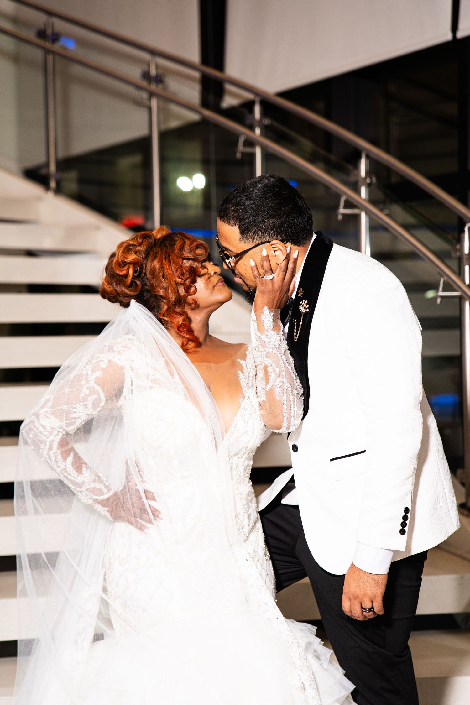 Romantic wedding moment captured on a modern staircase with flowing white lace dress details.