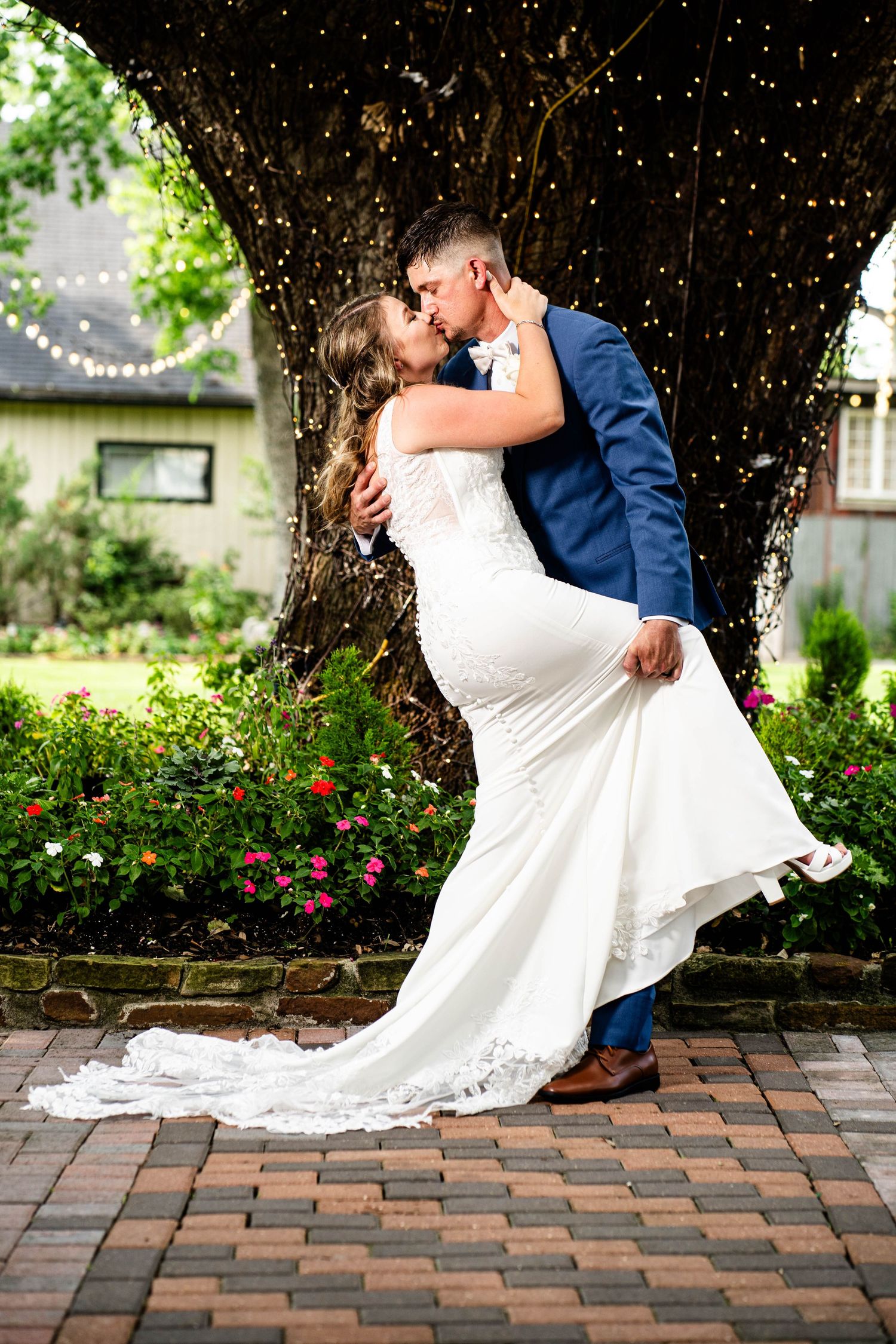 Romantic wedding photo of couple kissing under twinkling lights on brick patio.