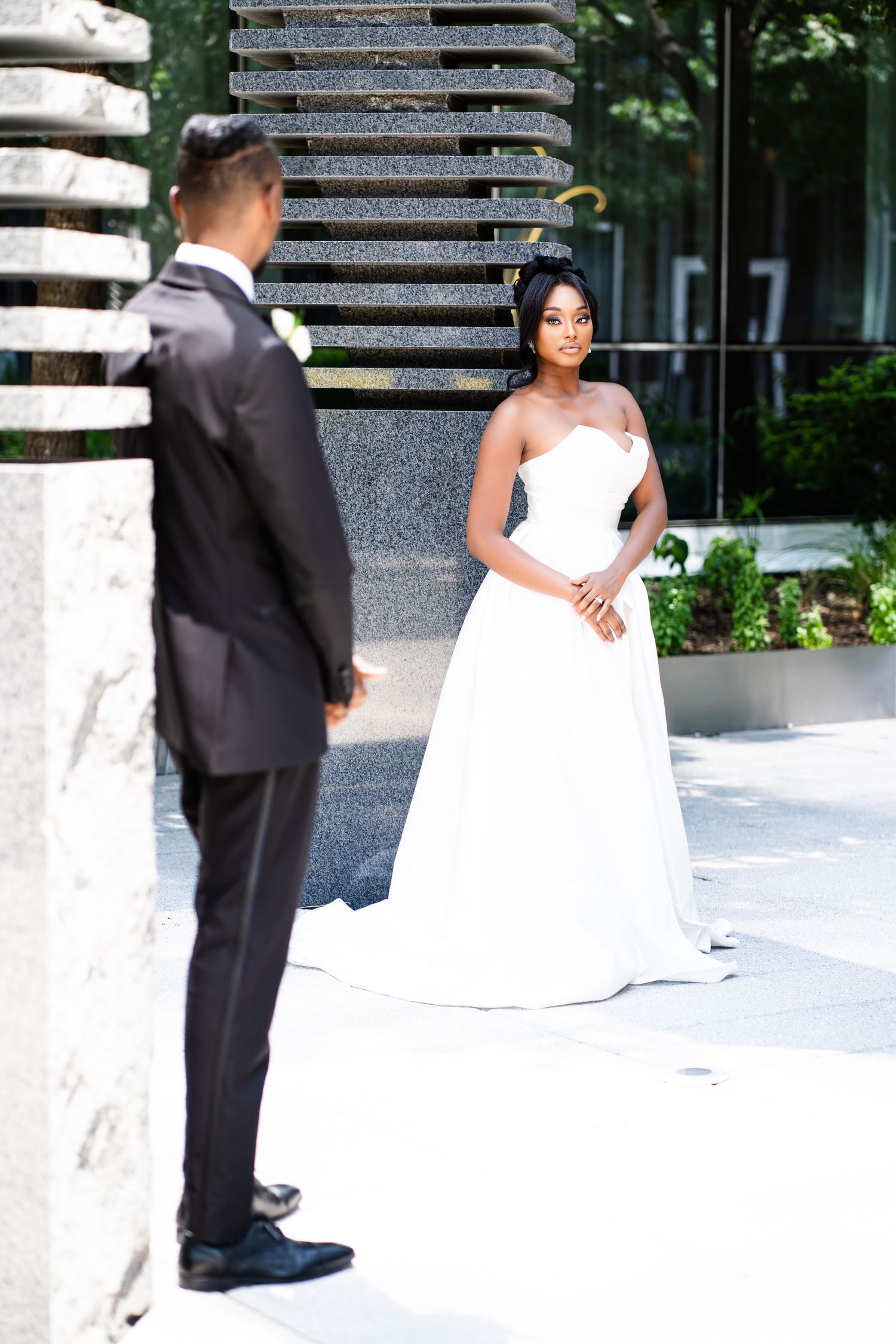 Wedding couple poses against modern stone columns in an outdoor setting.