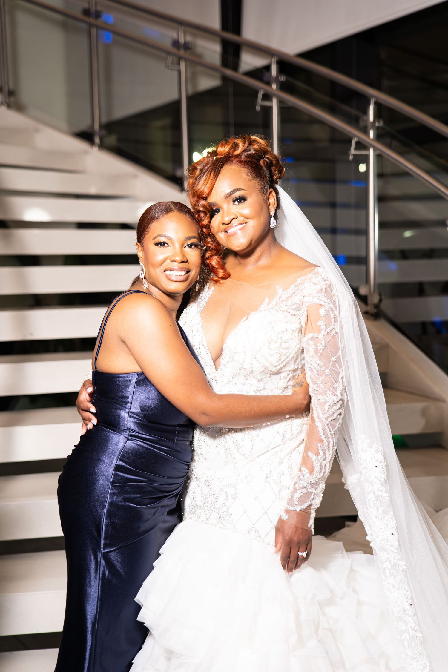 Emotional wedding moment captured between bride in white lace gown and bridesmaid in navy dress.