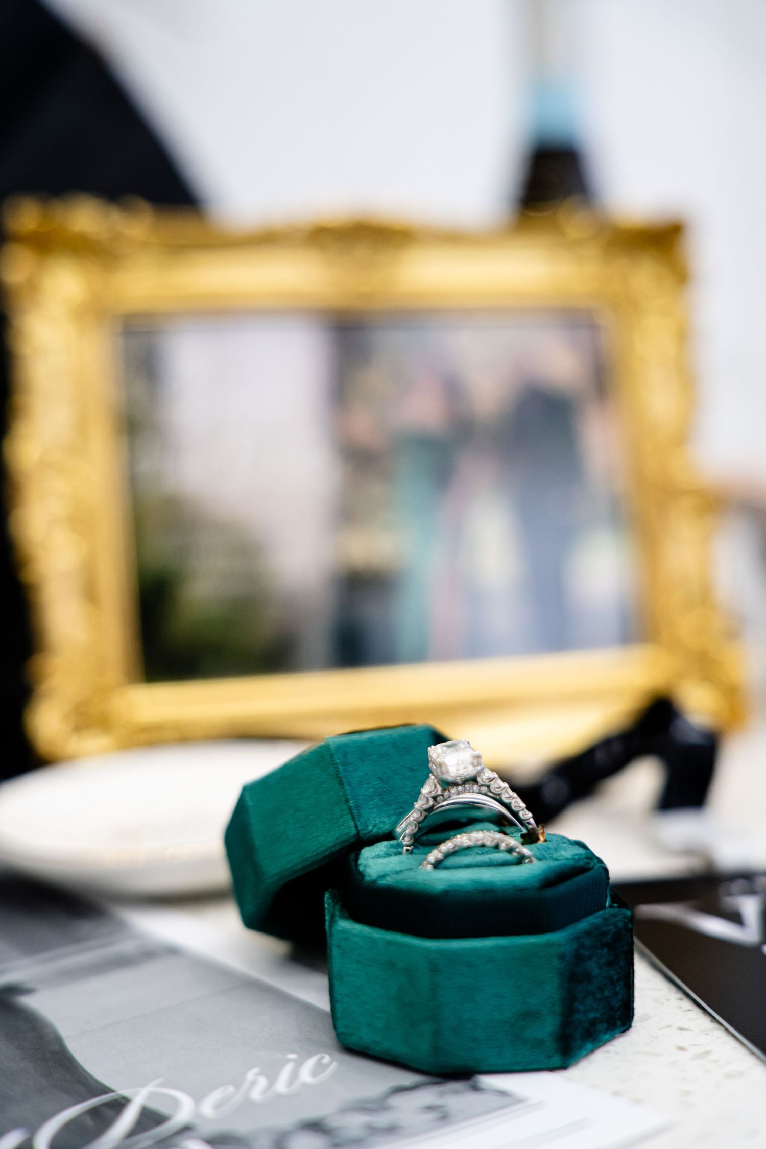 Engagement ring displayed on emerald green velvet ring box with gold frame in background.