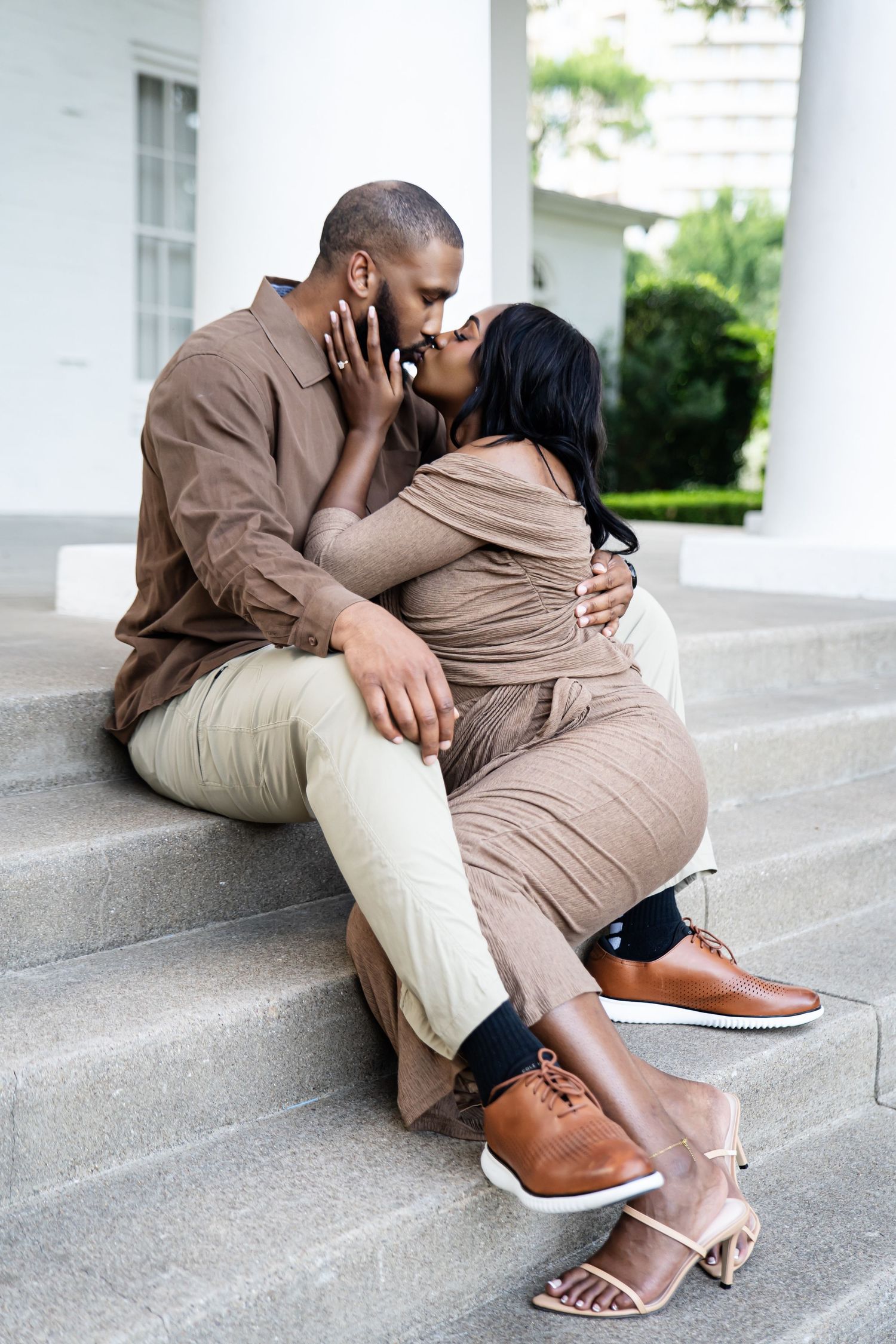 Romantic couple in matching brown outfits share an intimate moment on outdoor steps.