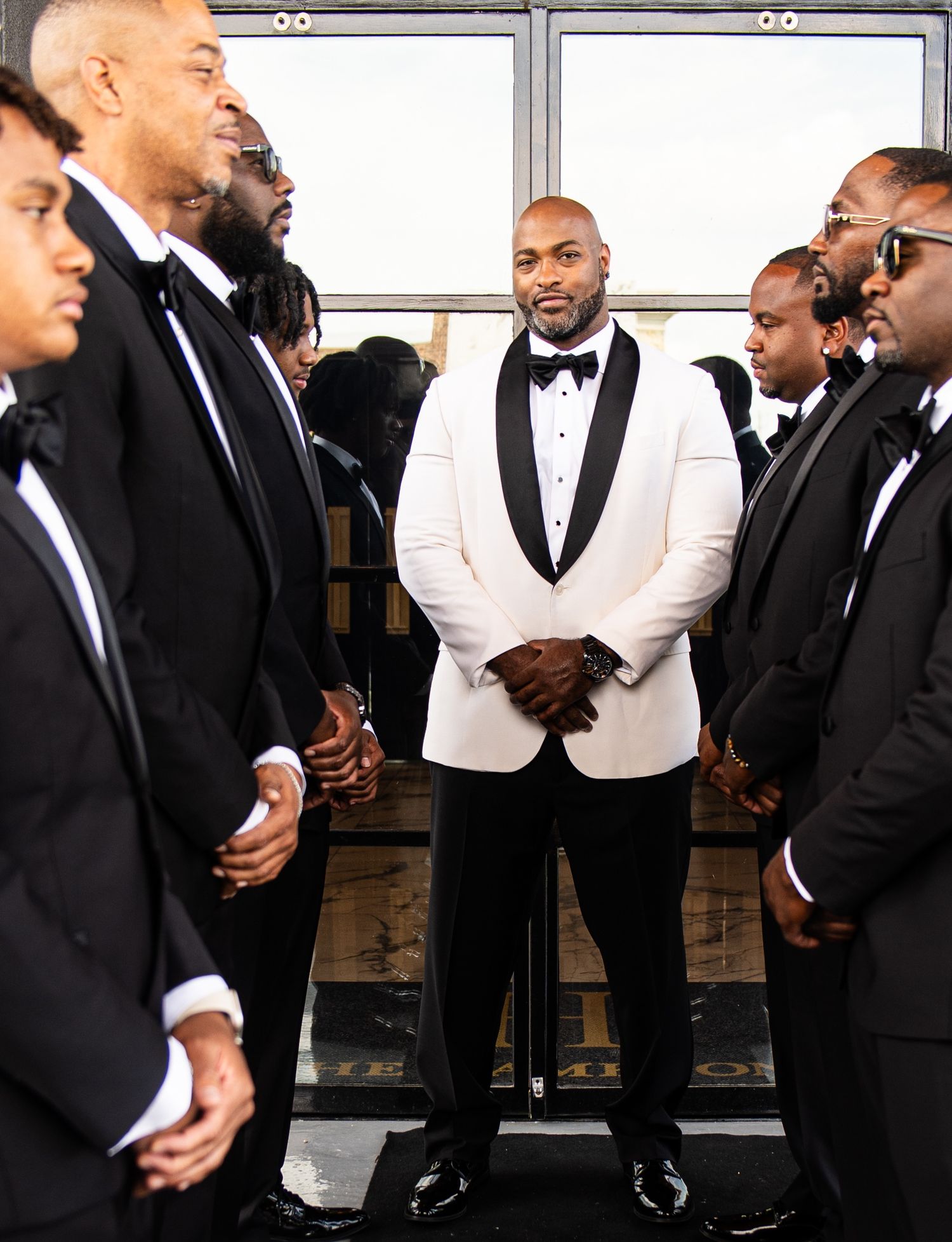 Groomsmen in black and white tuxedos gather for wedding photos.