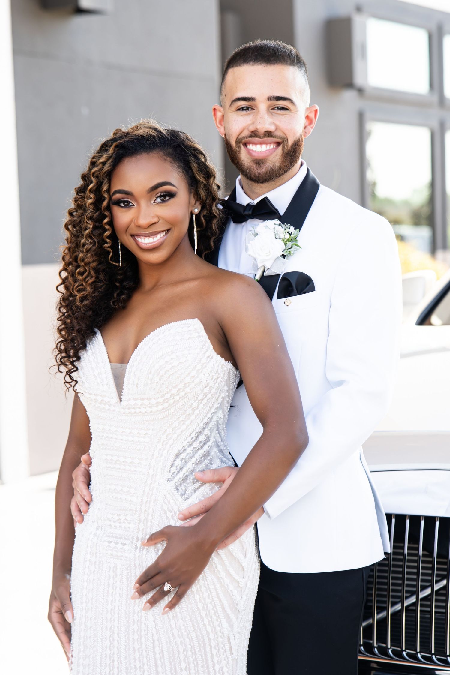 Happy newlyweds pose together in formal attire against a bright modern setting.