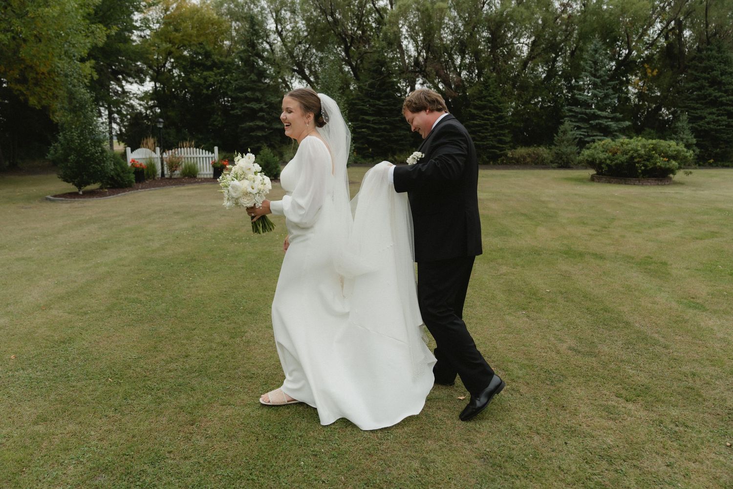 Wedding couple walking together across a scenic green lawn during their outdoor ceremony.