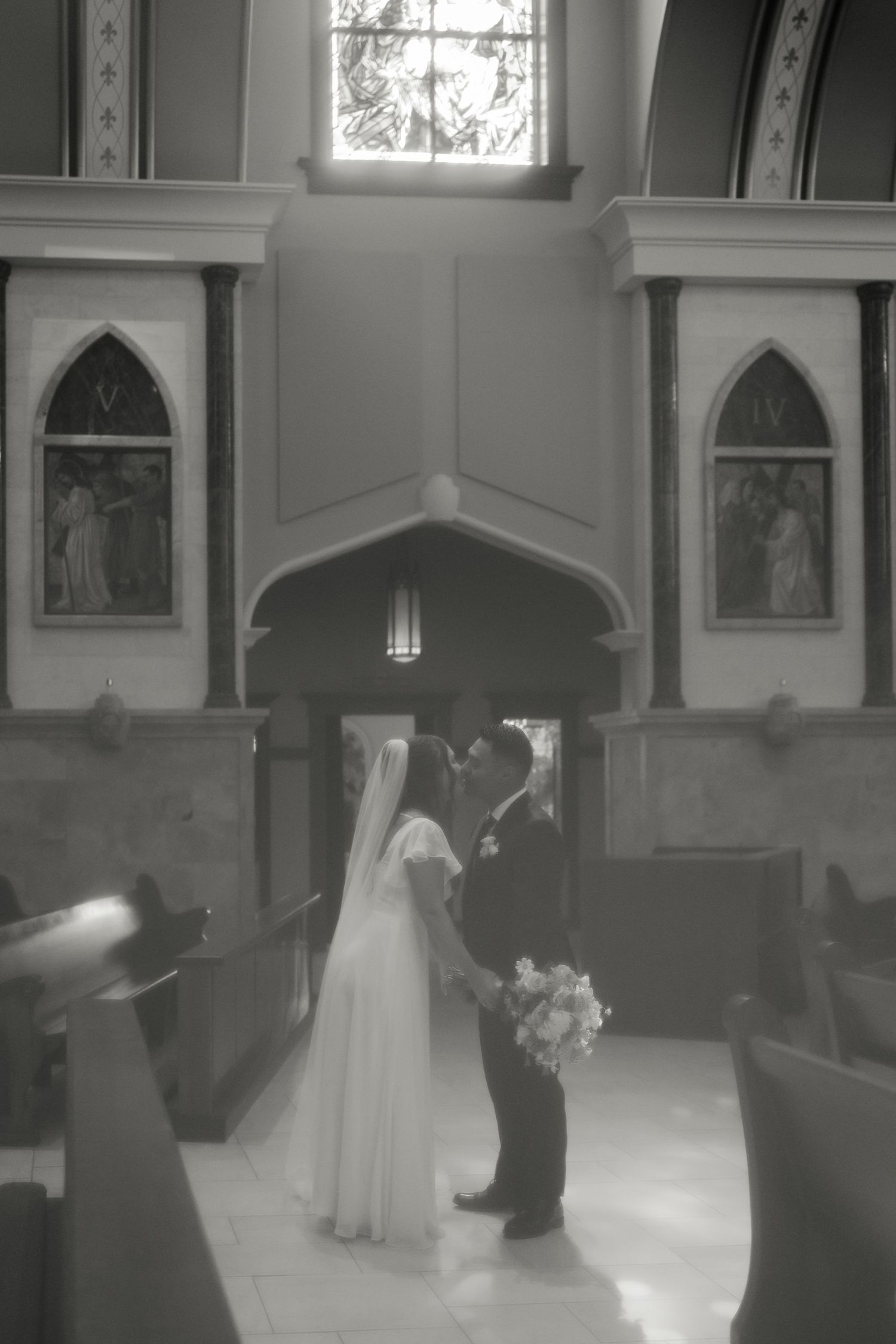 Black and white photo of bride and groom sharing first kiss at church altar during wedding ceremony.