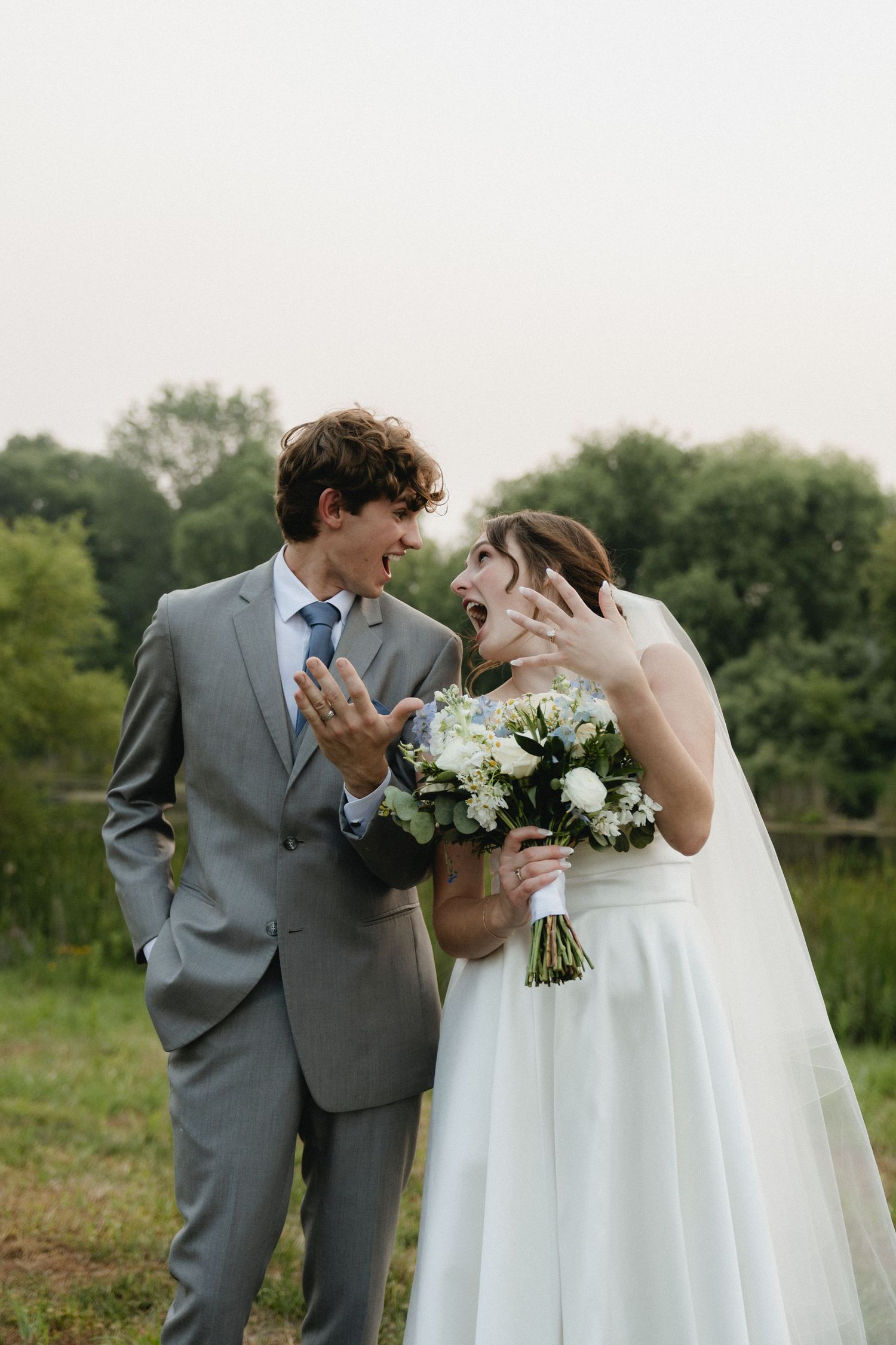 Wedding couple in grey suit and white dress sharing playful moments with flowers in a field.