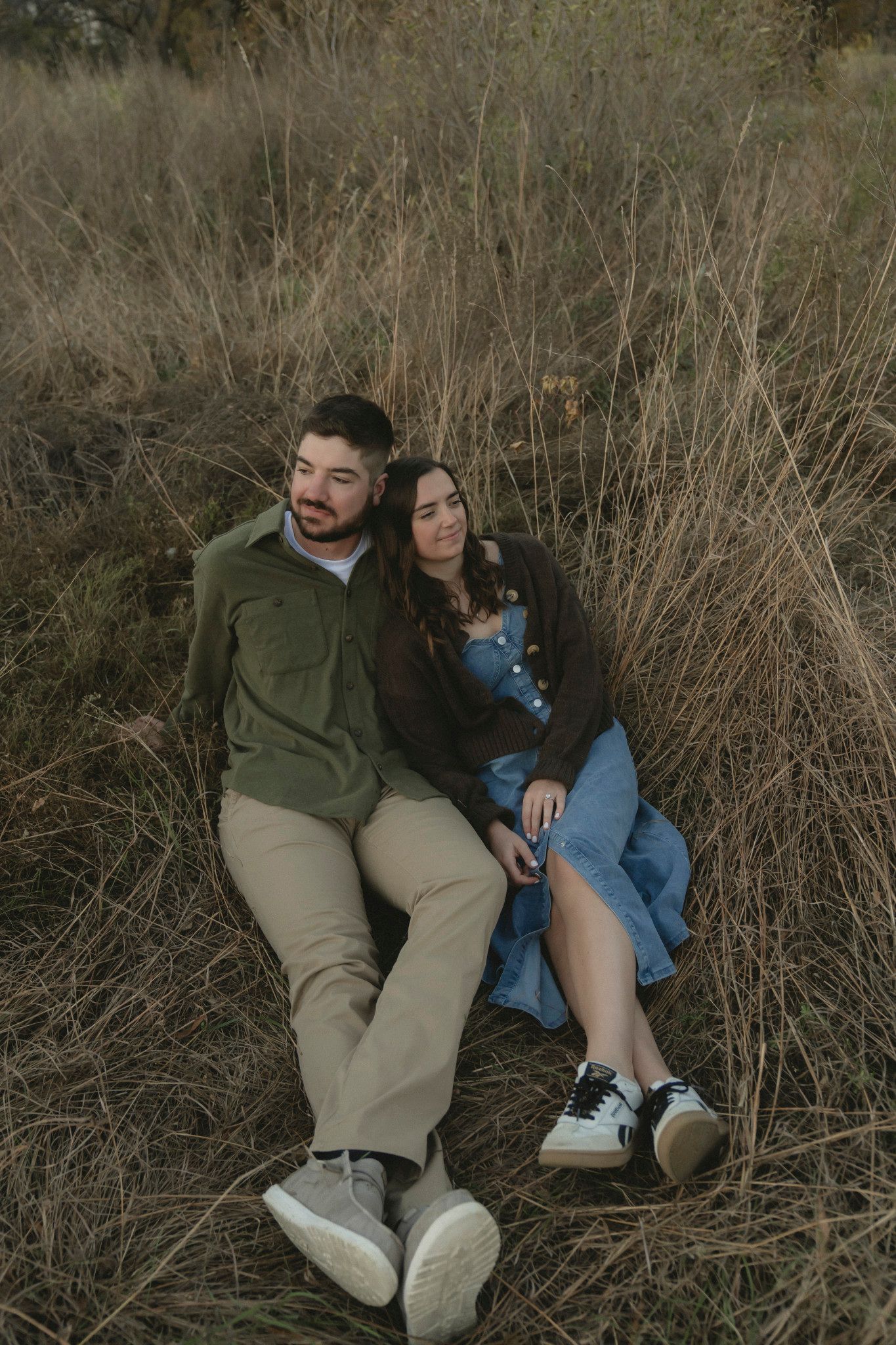 A couple relaxes together against tall dried grass during golden hour.