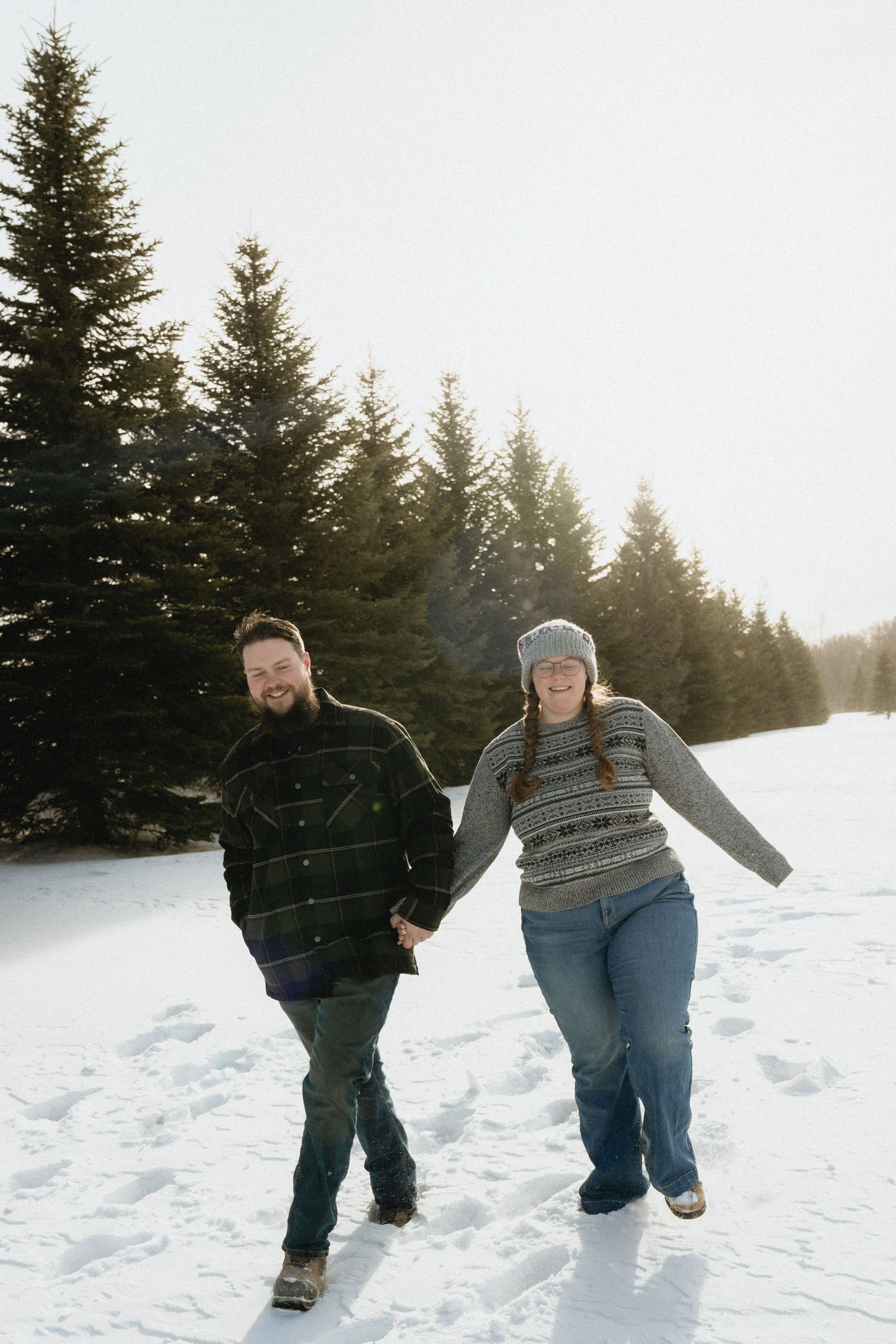 A couple holding hands while walking through snowy evergreen forest.
