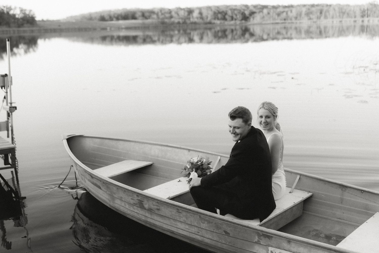 A vintage black and white photo shows a couple sitting in a rowboat on a calm lake.