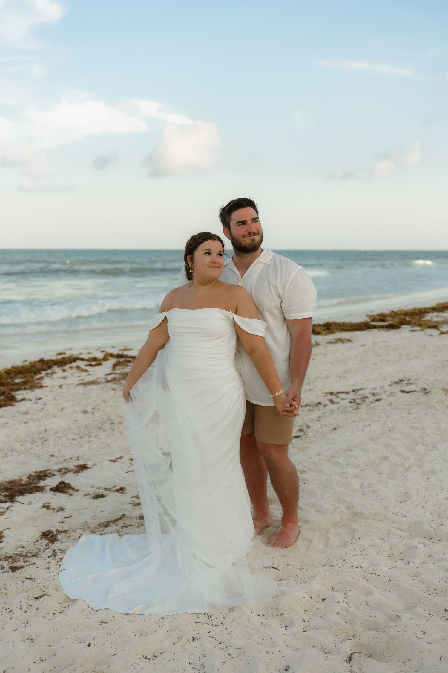 A couple sits together on a serene beach with white sand and blue skies during a romantic photoshoot.