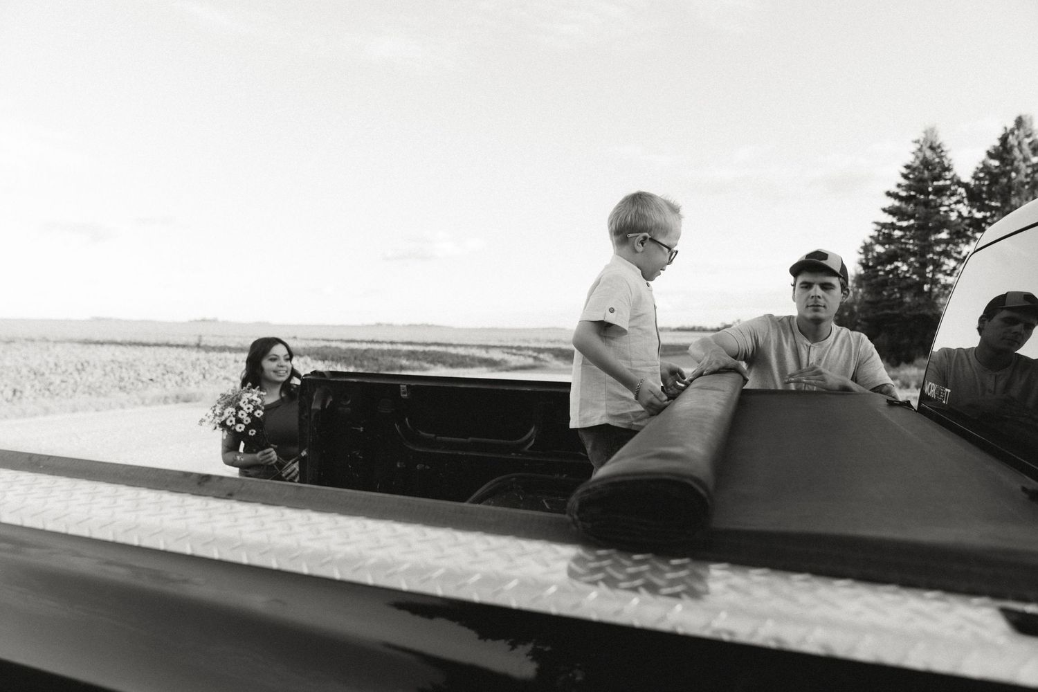 Black and white photo of people loading rolled material onto a truck bed in a rural landscape.
