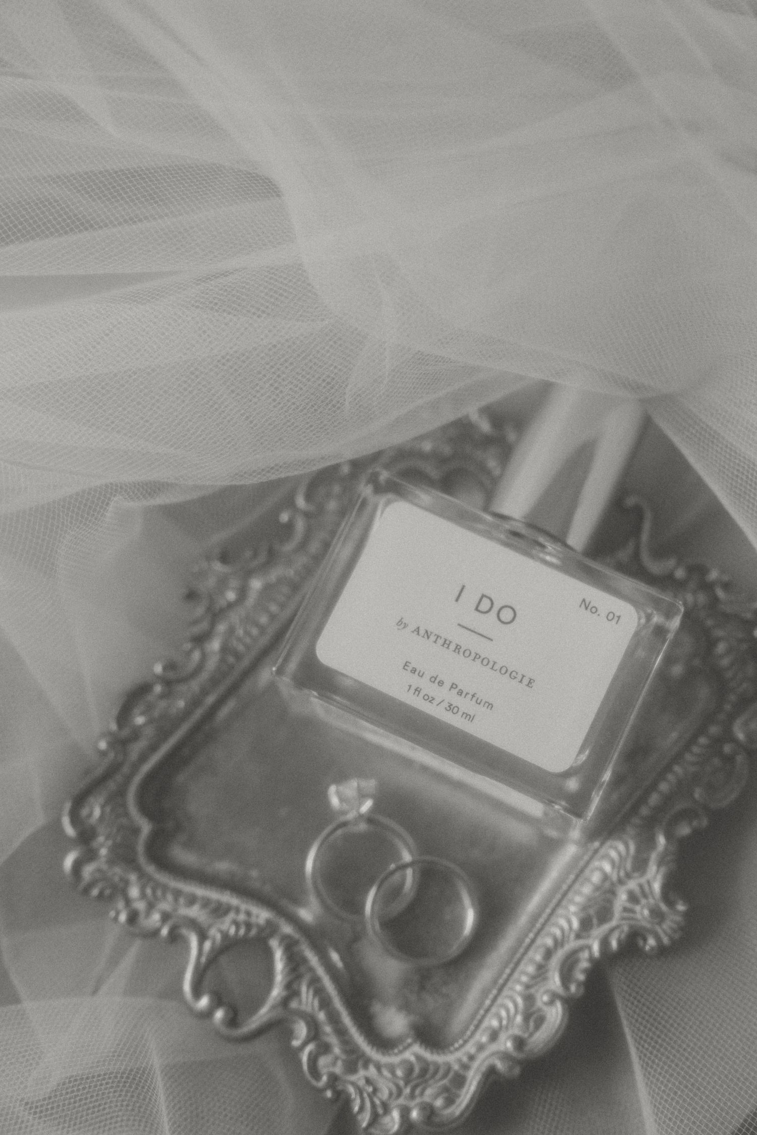 Wedding rings displayed on an ornate silver tray with 'I DO' text and delicate tulle overlay.